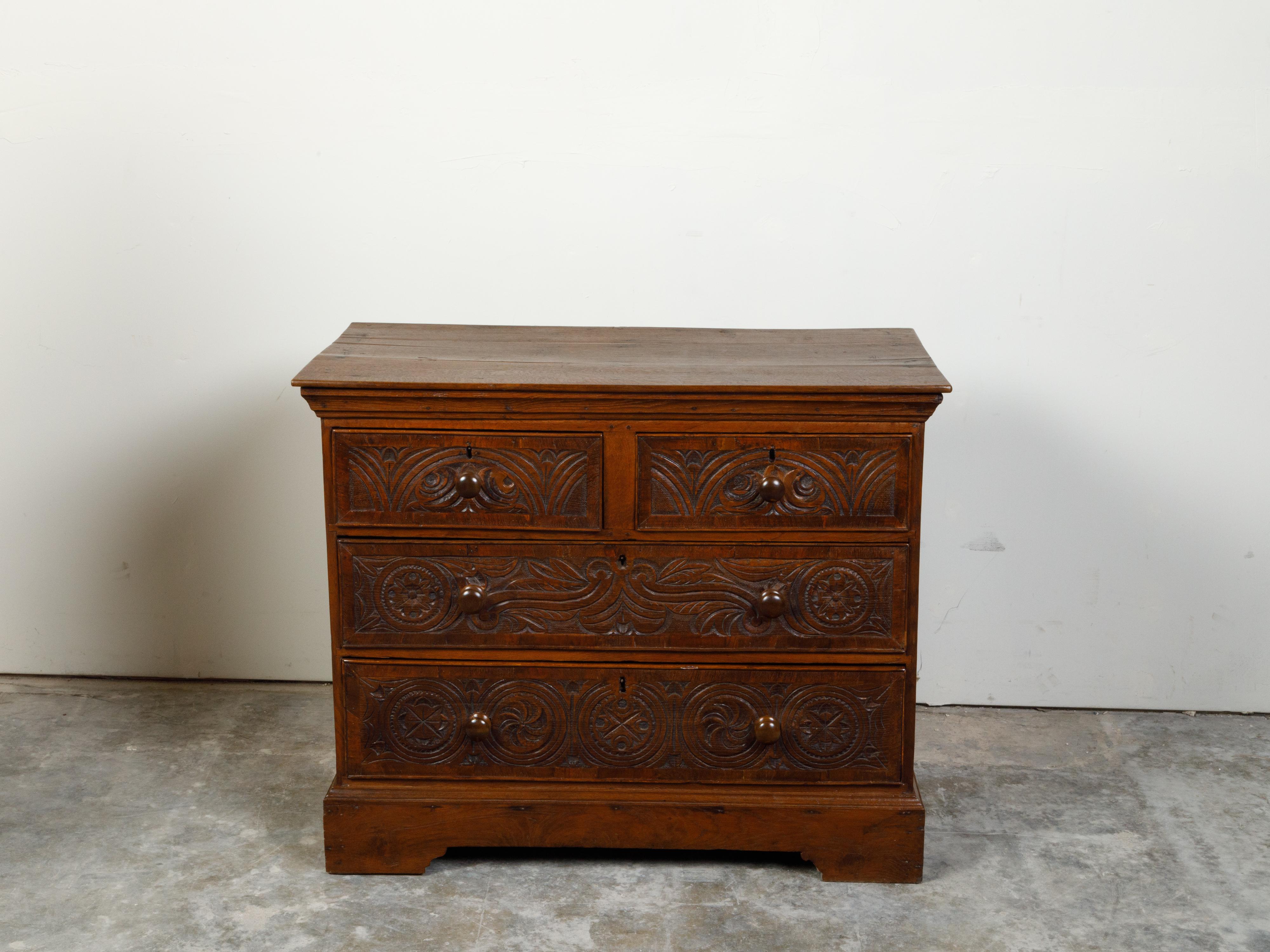 An English Georgian period oak chest from the early 19th century, with four drawers and carved motifs. Created in England during the early years of the 20th century, this oak chest features a rectangular top sitting above two small drawers followed