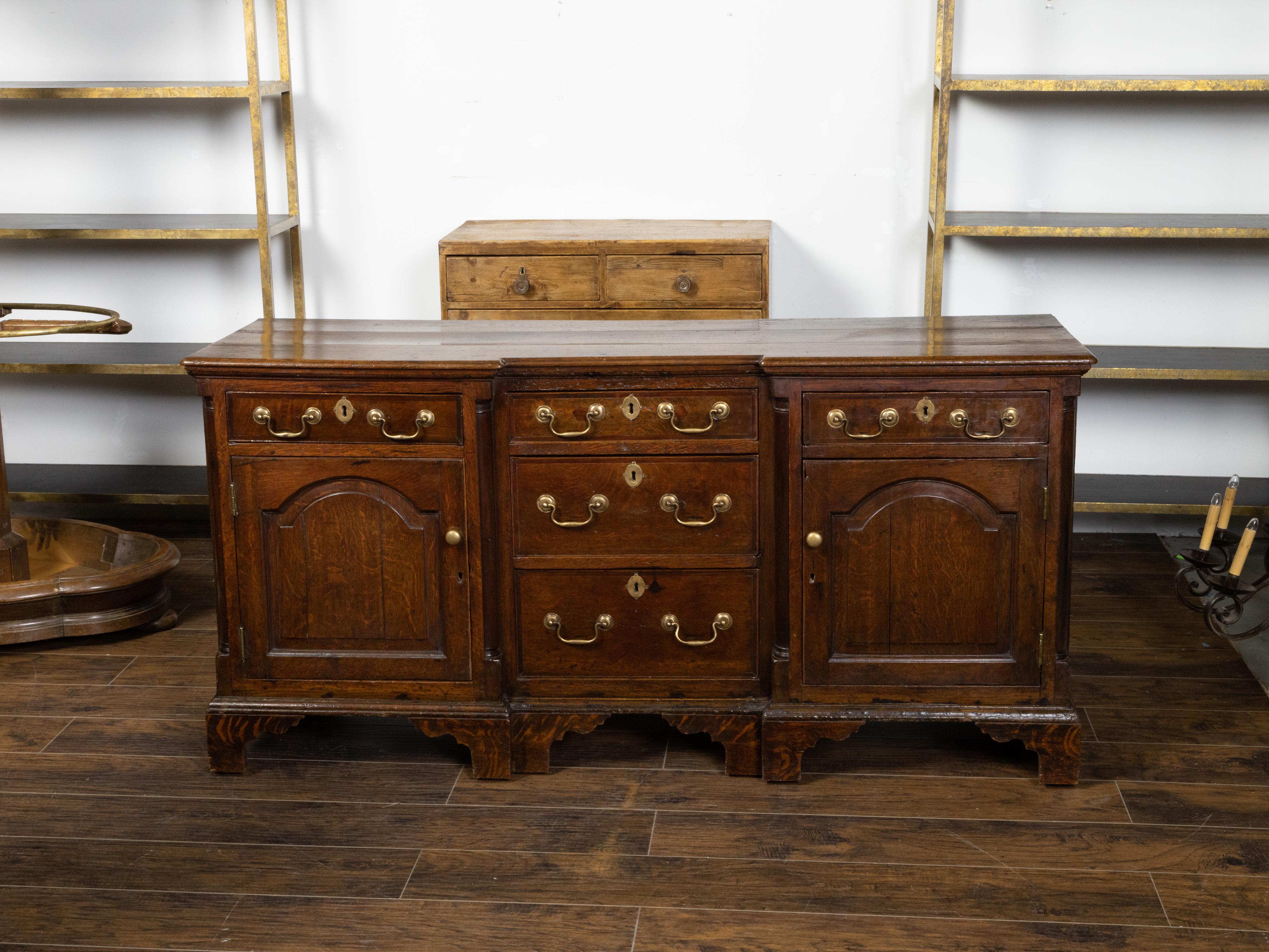 An English Georgian period oak dresser base from the early 19th century, with five drawers, two doors, brass hardware and veneered bracket feet. Created in England during the Georgian period in the early years of the 19th century, this oak piece,