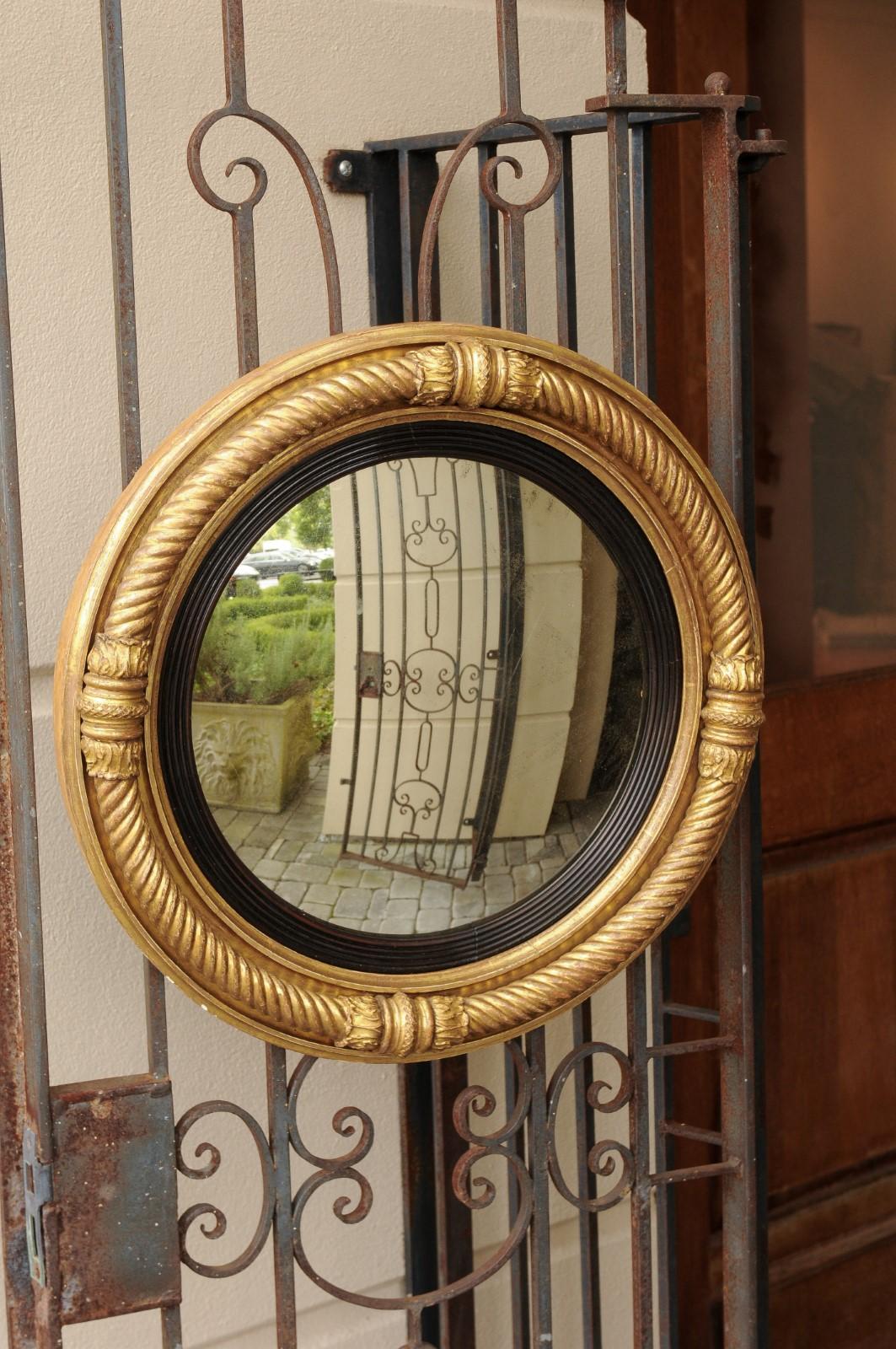 An English Georgian period giltwood convex mirror from the early 19th century, with ebonized accents and twisted rope motifs. This exquisite English mirror features a convex mirror plate, surrounded by an inner ebonized molded frame. The outer frame
