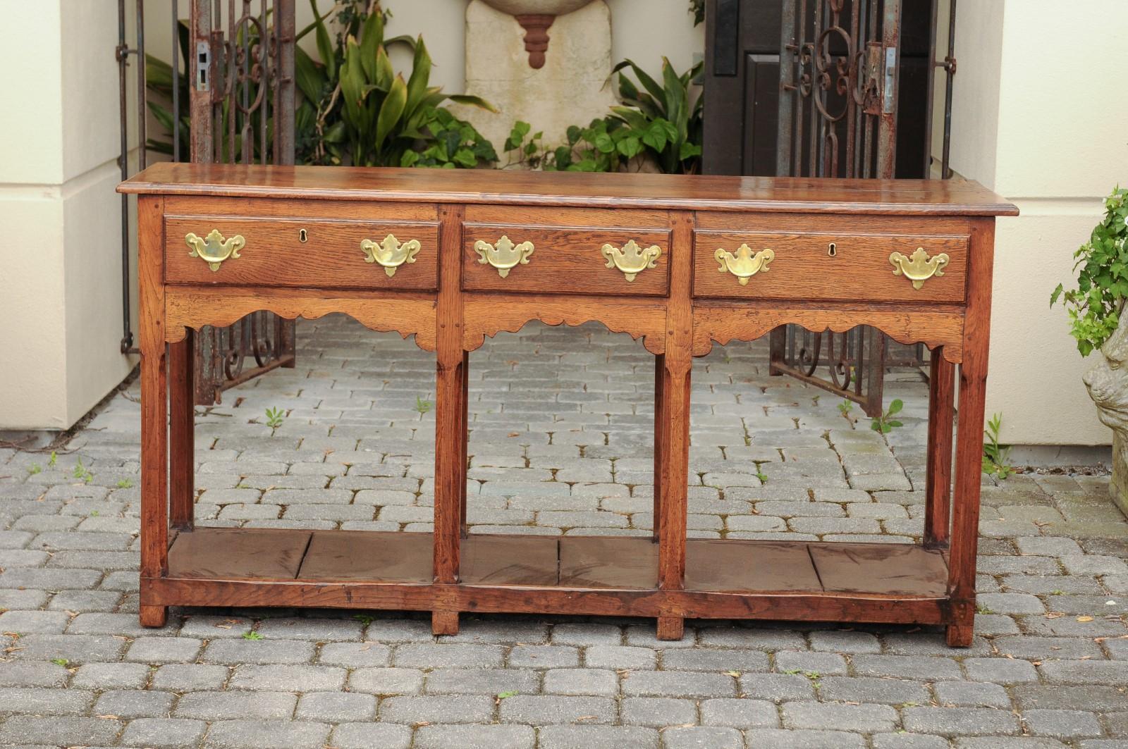 An English Georgian period oak dresser base from the early 19th century, with three drawers, scalloped apron and pot board base. Born in England during the reign of King George IV, this elegant dresser base features a rectangular planked top sitting