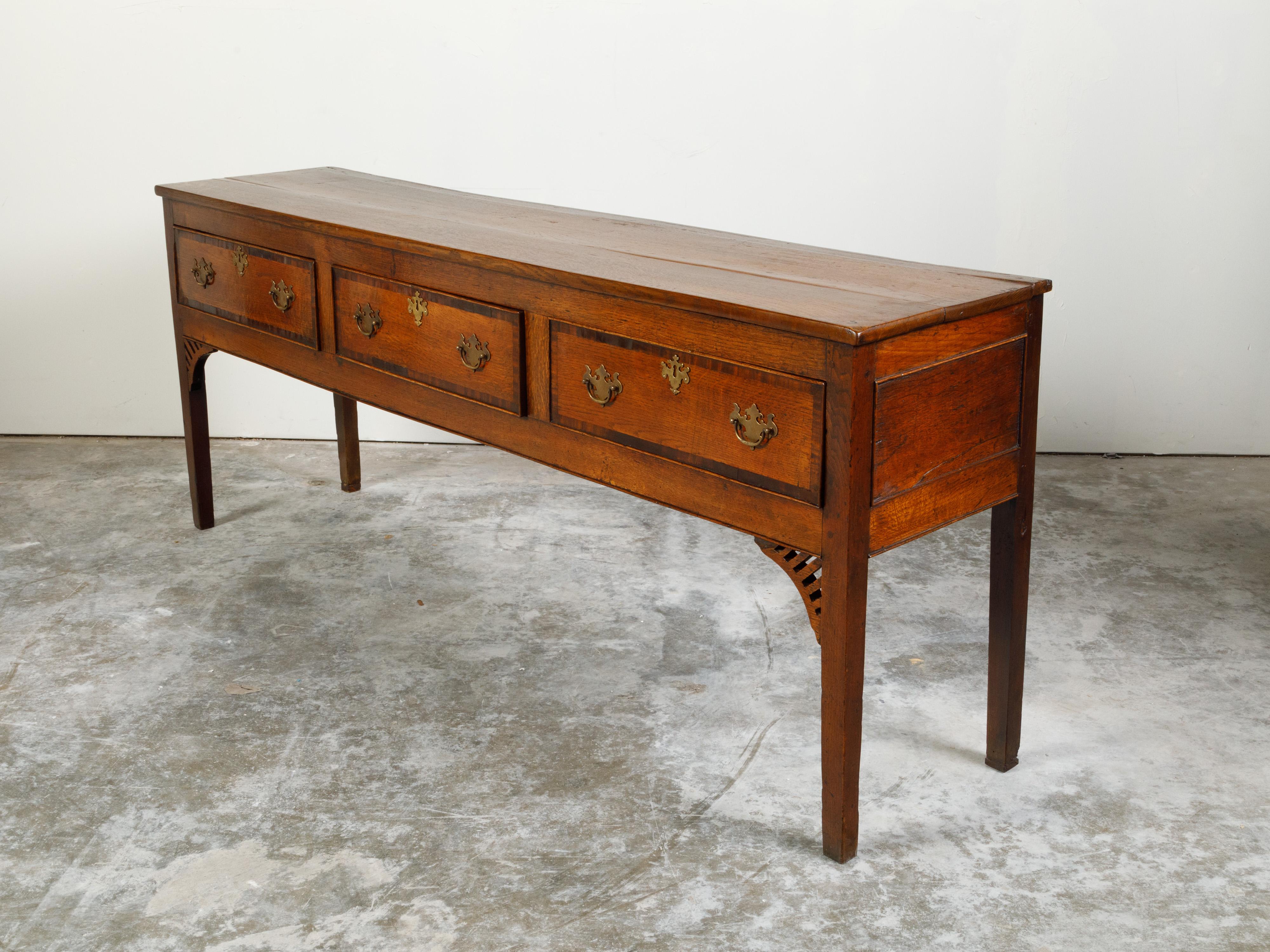 An English Georgian period oak sideboard from the early 19th century, with three drawers, banding and brass Chippendale style hardware. Created in England during the first quarter of the 19th century, this oak sideboard features a rectangular top