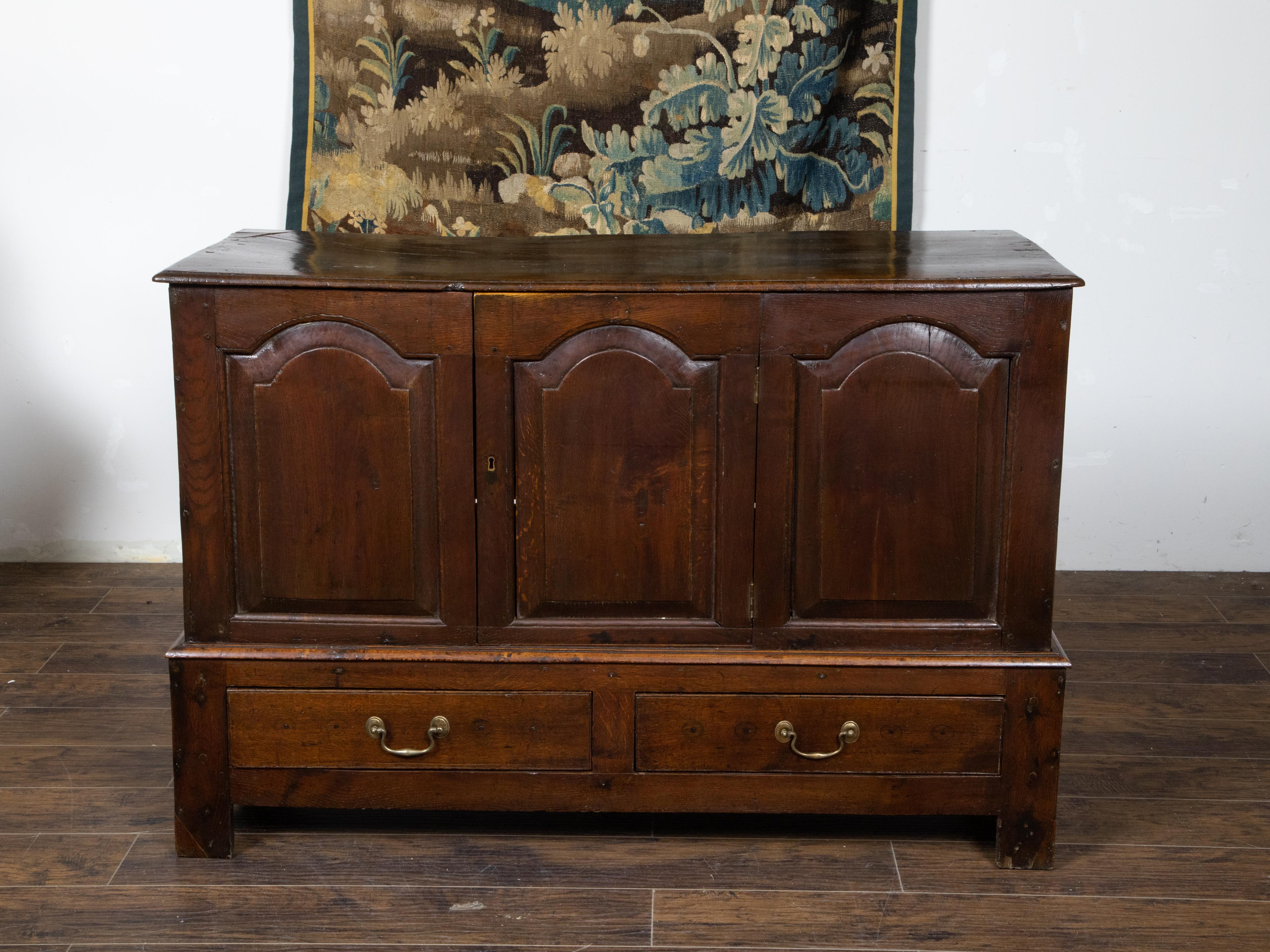 An English Georgian period oak buffet from the 18th century, with single central door, two drawers, carved arching motifs and brass hardware. Created in England during the Georgian era in the 18th century, this oak buffet features a rectangular top