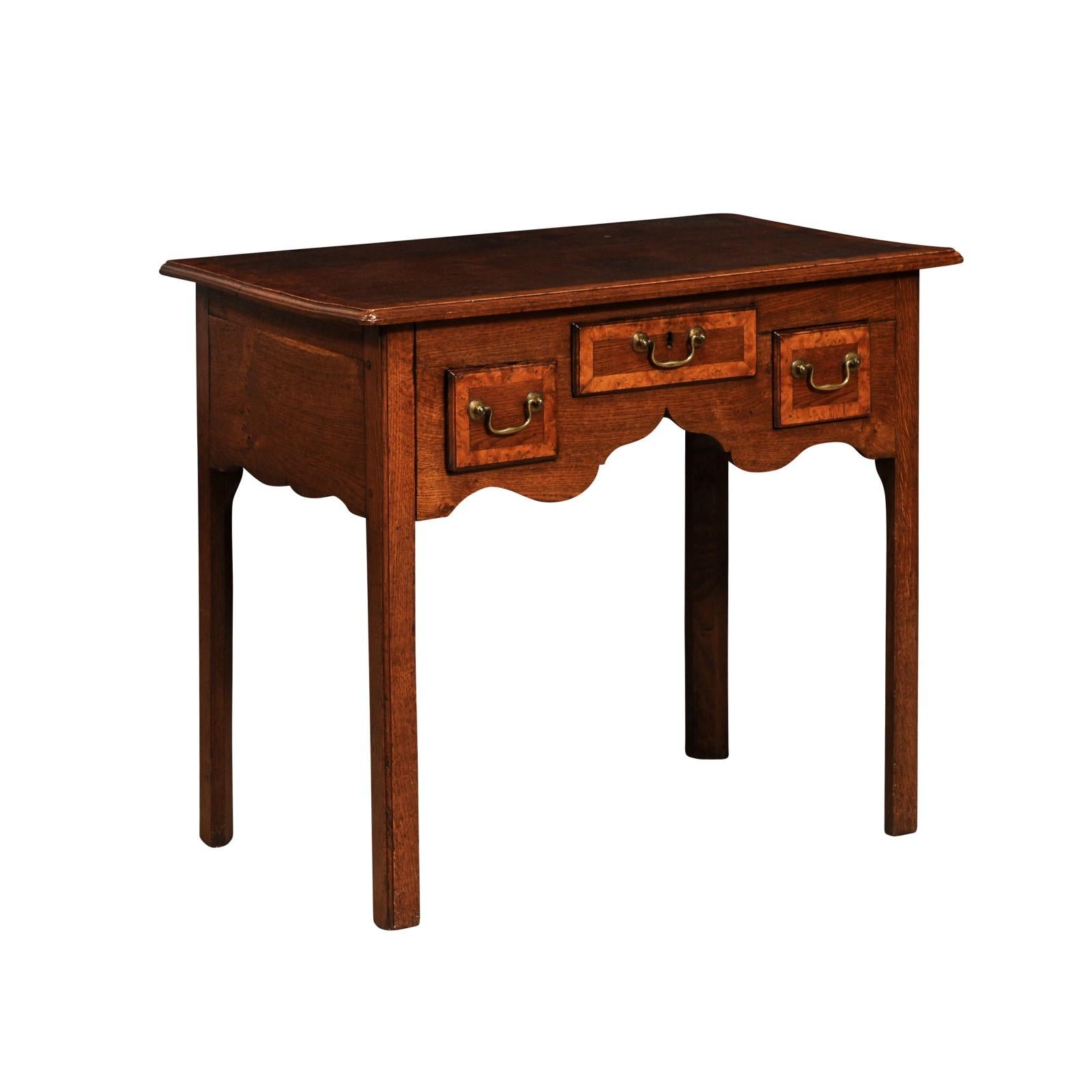 An English Georgian period oak lowboy side table from the 18th century with three drawers, carved apron, cross-banded accents and straight legs. This English Georgian period oak lowboy side table, dating back to the 18th century, is a classic piece,