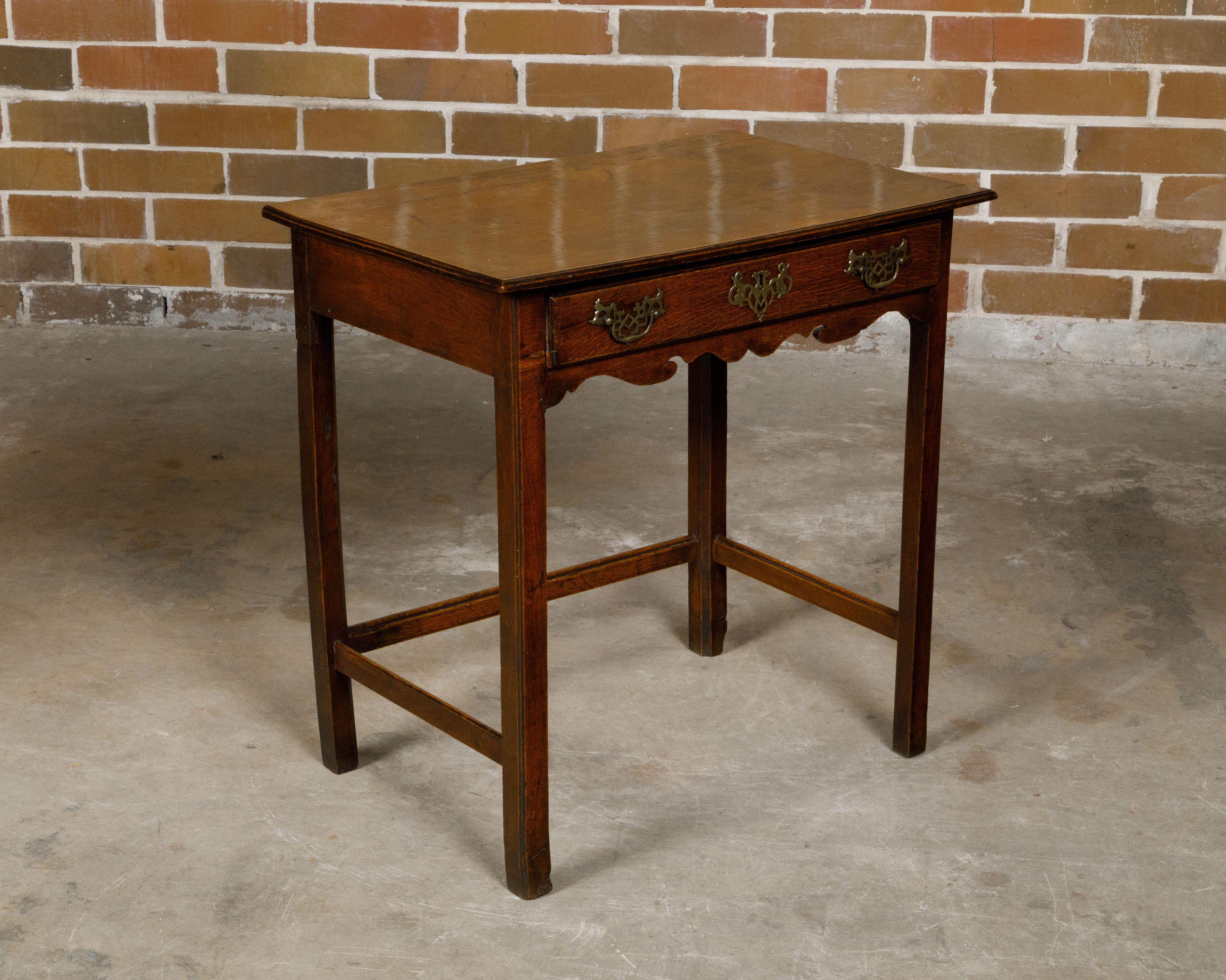 An English Georgian period oak side table from the 18th century with single drawer, carved apron and brass Chippendale style hardware. Born in England during the 18th century, this exquisite Georgian period oak side table features a single drawer