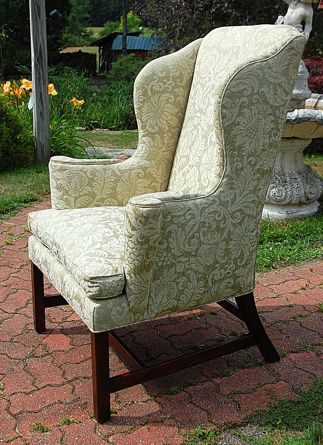 English Georgian period Chippendale mahogany wing chair with square molded legs. This particularly stylish wing chair has an H-stretcher, out swept arms, shaped tall back, serpentine shaped wings, loose cushion. The
roll of the out swept arms and