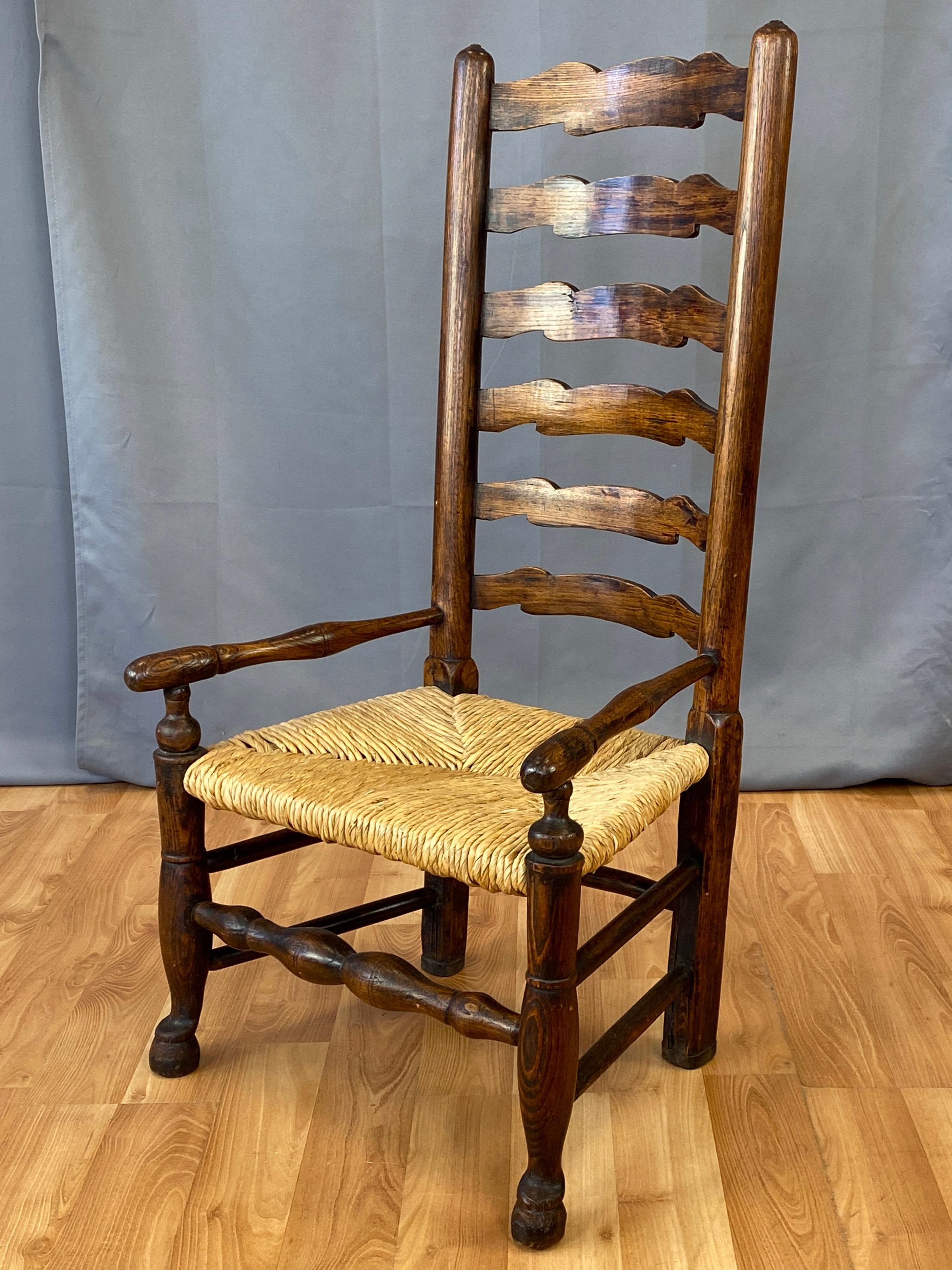 An uncommon circa 1800 English Georgian period country ladderback fireside armchair in elm with woven rush seat.

Delightfully proportioned, with the tall six-slat back “towering” over the extra-low seat, and the frame having a laid-back profile.