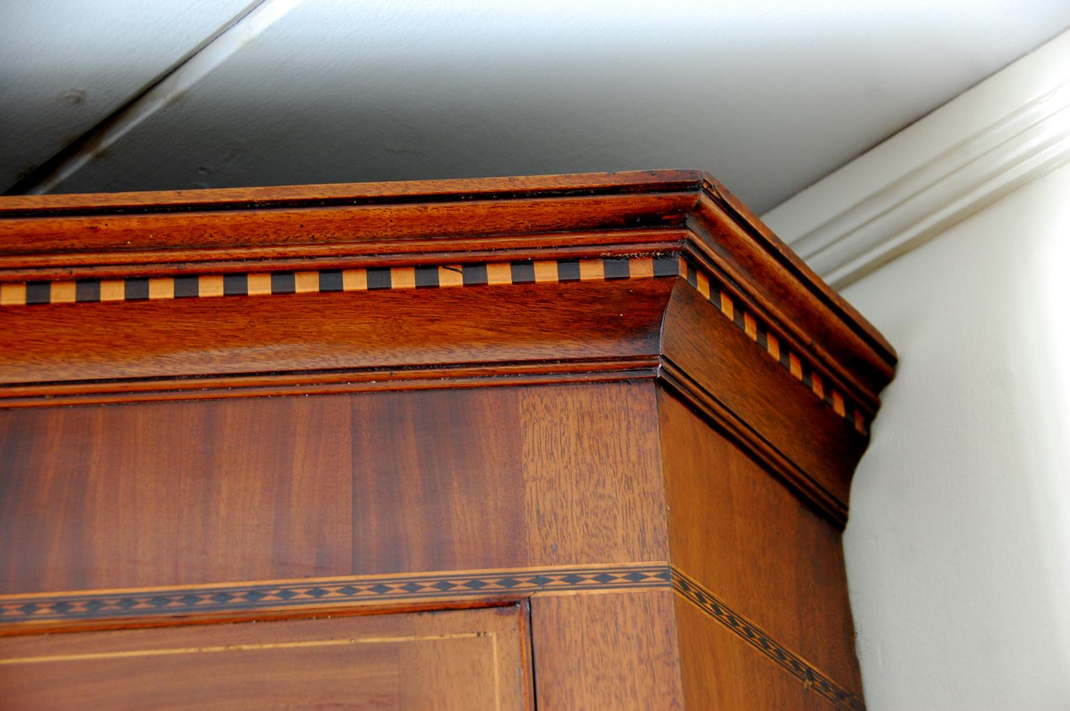 English Georgian period Hepplewhite inlaid mahogany hanging corner cupboard with boxwood stringing to muntins and door. At the cornice there is dentil molding in alternating boxwood and mahogany, as well as more elaborate stringing on the frieze,