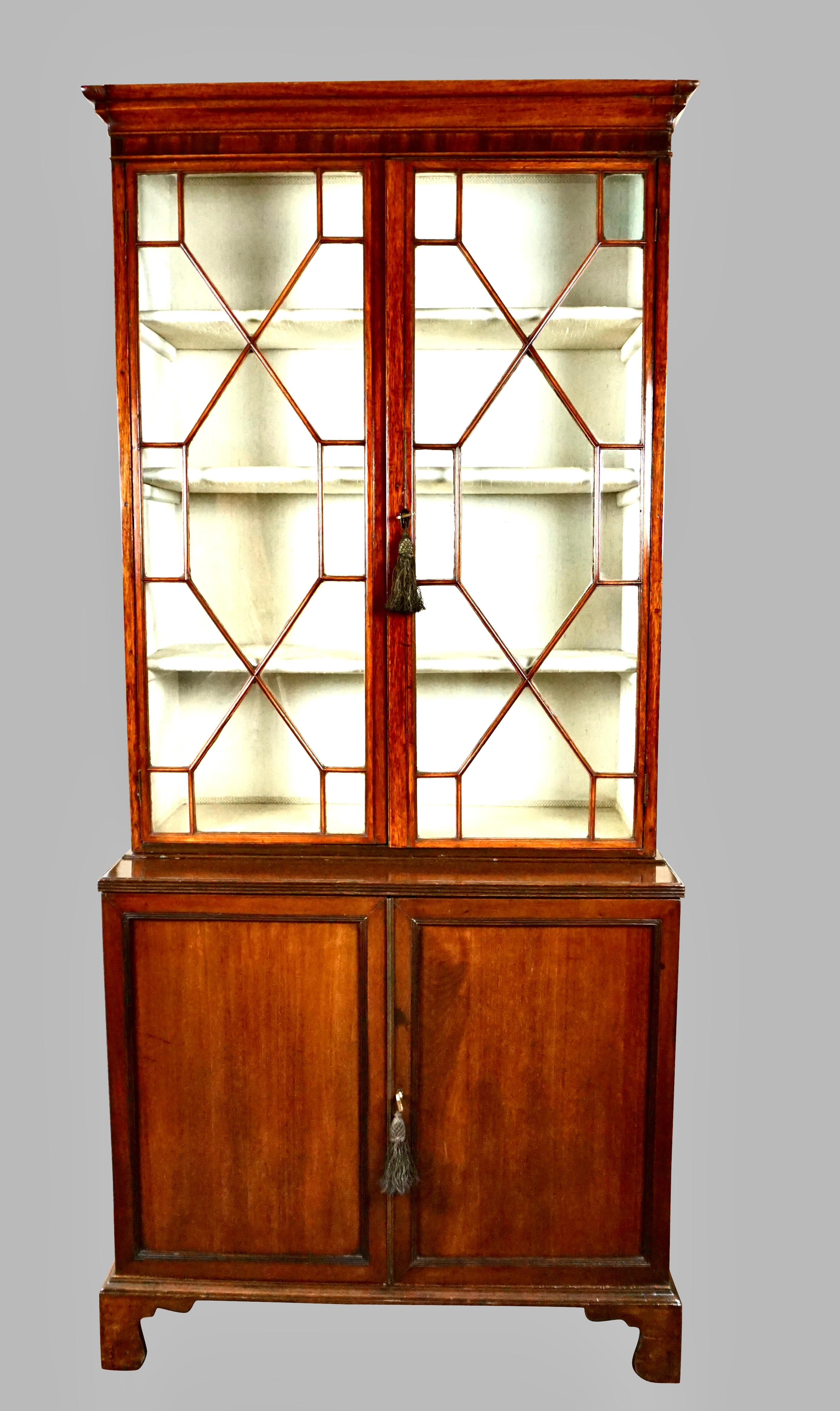An English Georgian period mahogany bookcase, the glazed upper section now lined in fabric, above 2 cabinet doors, all supported on bracket feet. A simple but very elegant and useful piece of period English furniture in attractive overall condition.