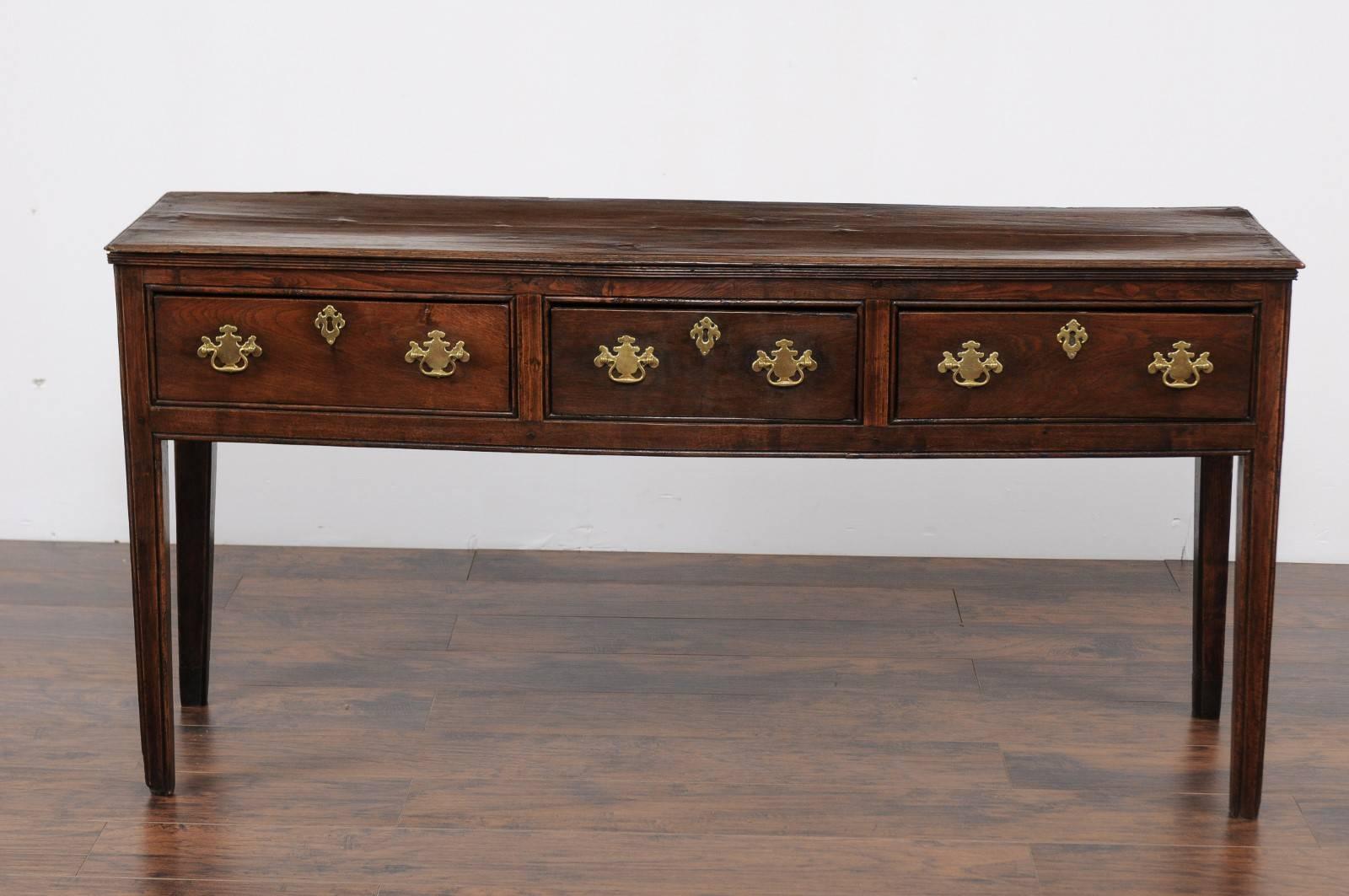 An English Georgian period oak dresser base from the early 19th century with three drawers and straight legs. This exquisite server was born during the reign of King George III of England. Featuring a rectangular planked top with a delicately reeded