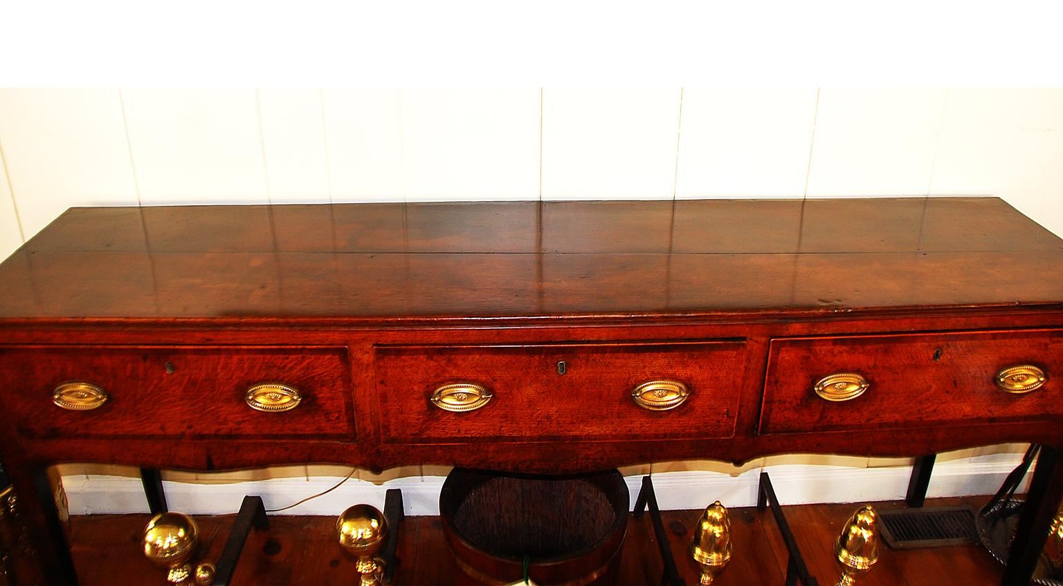 English Georgian period oak low dresser with shaped skirt; mahogany crossbanding and boxwood stringing to the three drawers; tapered legs, circa 1790.