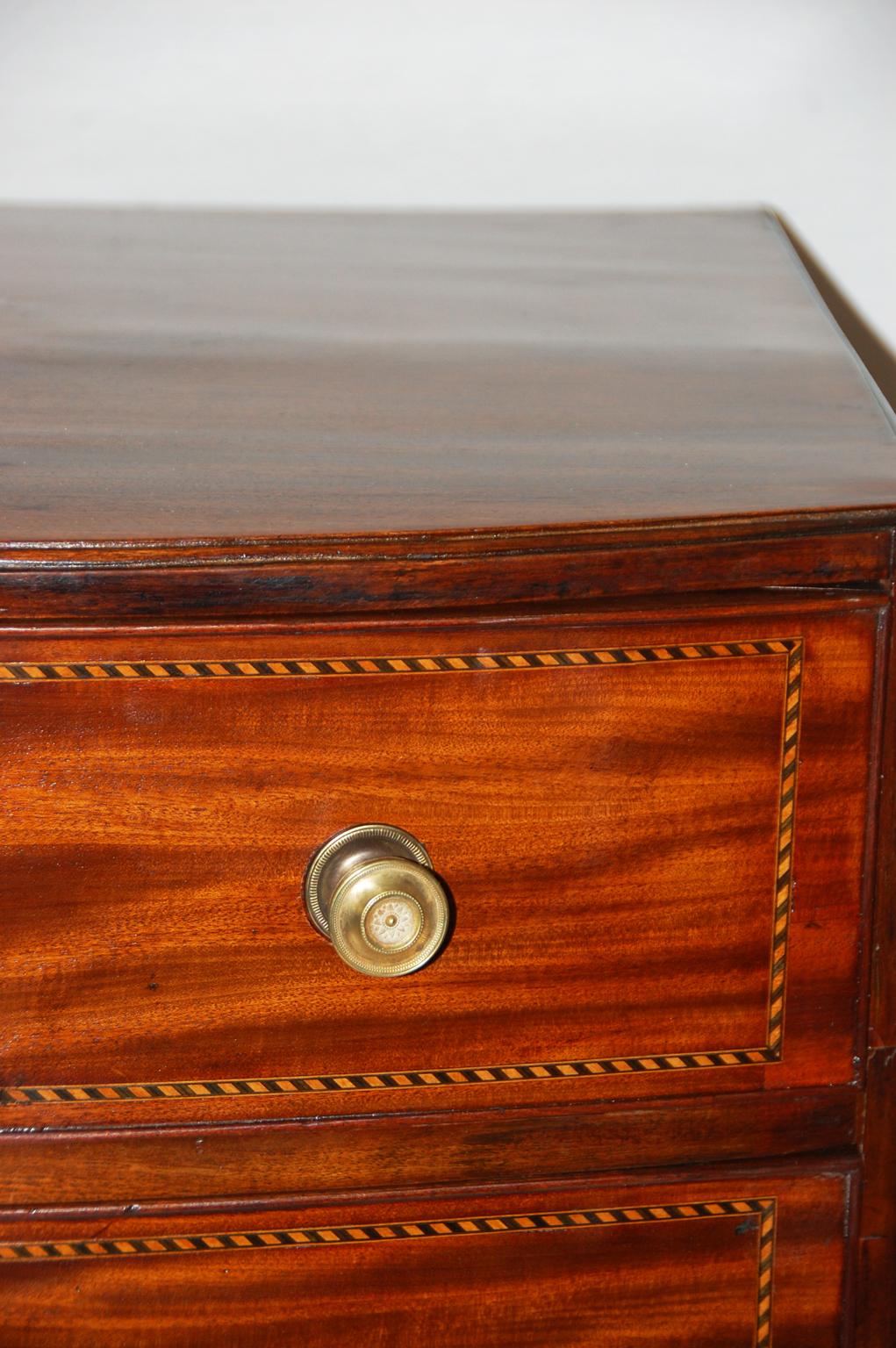 English diminutive Georgian period Hepplewhite bowfront mahogany chest of three graduated drawers with satinwood and ebony stringing, French splay feet, shaped skirt, molded edges, inlaid bone escutcheons. At 27 Inches wide, this quite small chest