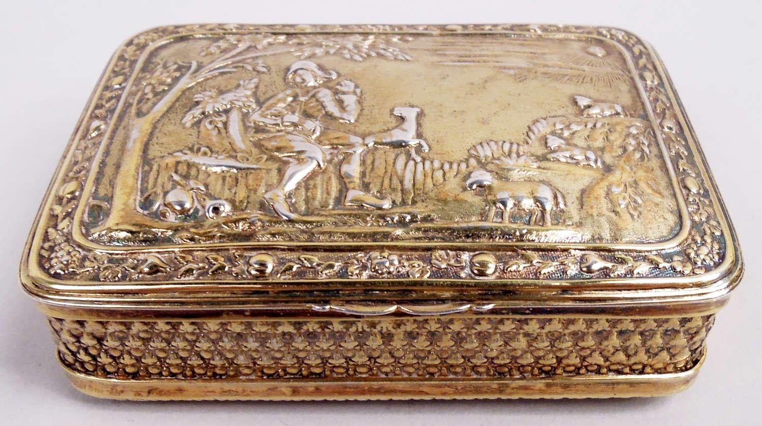 Tabaquera inglesa georgiana de plata de ley dorada, 1812. Rectangular con lados rectos. Portada abisagrada y con lengüetas; en la parte superior, escena pastoral cincelada: Un pastor sentado bajo un árbol con un cordero en brazos mientras los demás
