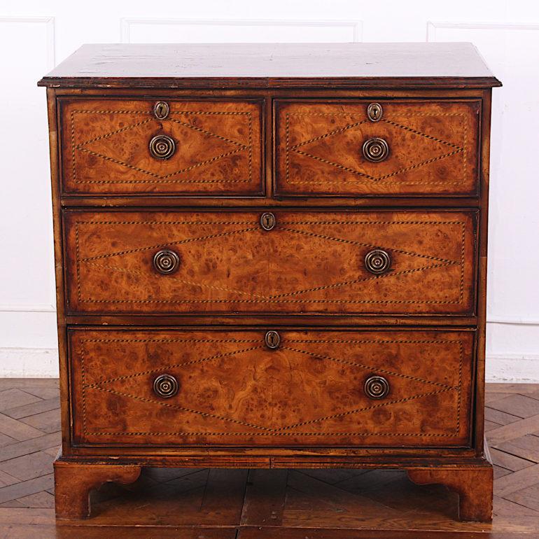 An English Georgian-revival chest of drawers with two short over two long drawers, the case with highly-figured book-matched yew wood veneer with ebony and boxwood inlay, the drawers with brass pulls and escutcheons, the whole raised on square