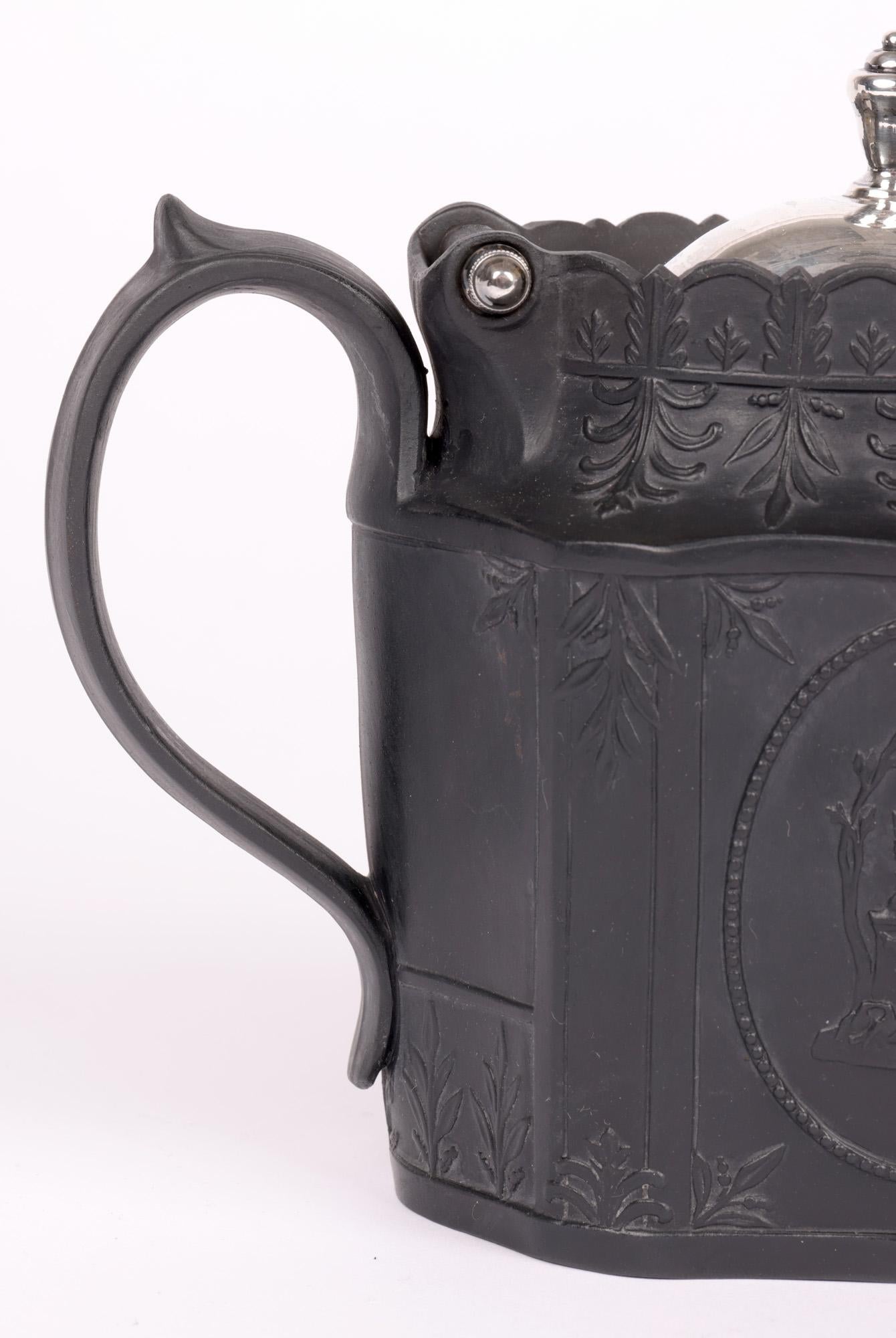 A finely made English Georgian later silver mounted black basalt teapot decorated with classical winged cherub designs to either side and dating from around 1810. The teapot has a decagon shaped body with a large raised loop pouring handle with
