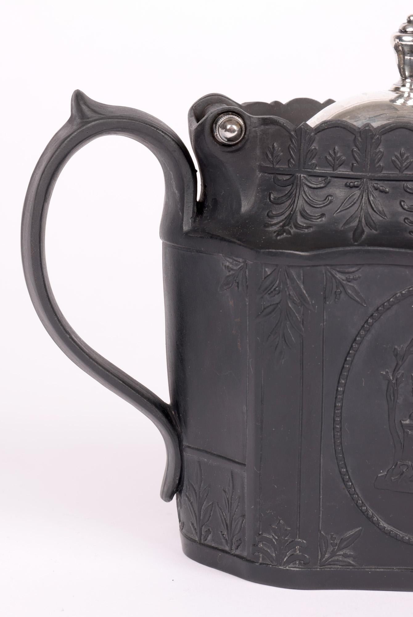 Una teiera in basalto nero di epoca georgiana finemente lavorata e montata in argento, decorata con disegni classici di cherubini alati su entrambi i lati e risalente al 1810 circa. La teiera ha un corpo a forma di decagono con un grande manico ad