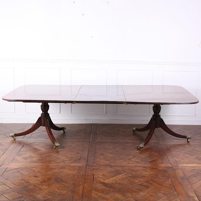 A George III solid Cuban mahogany twin-pillar dining table with original single plank leaf, the turned column supports raised on sabre legs terminating in the original ‘hairy paw’ brass castors. 

75 inches Wide x 54.5 inches Deep x 28 inches Tall.