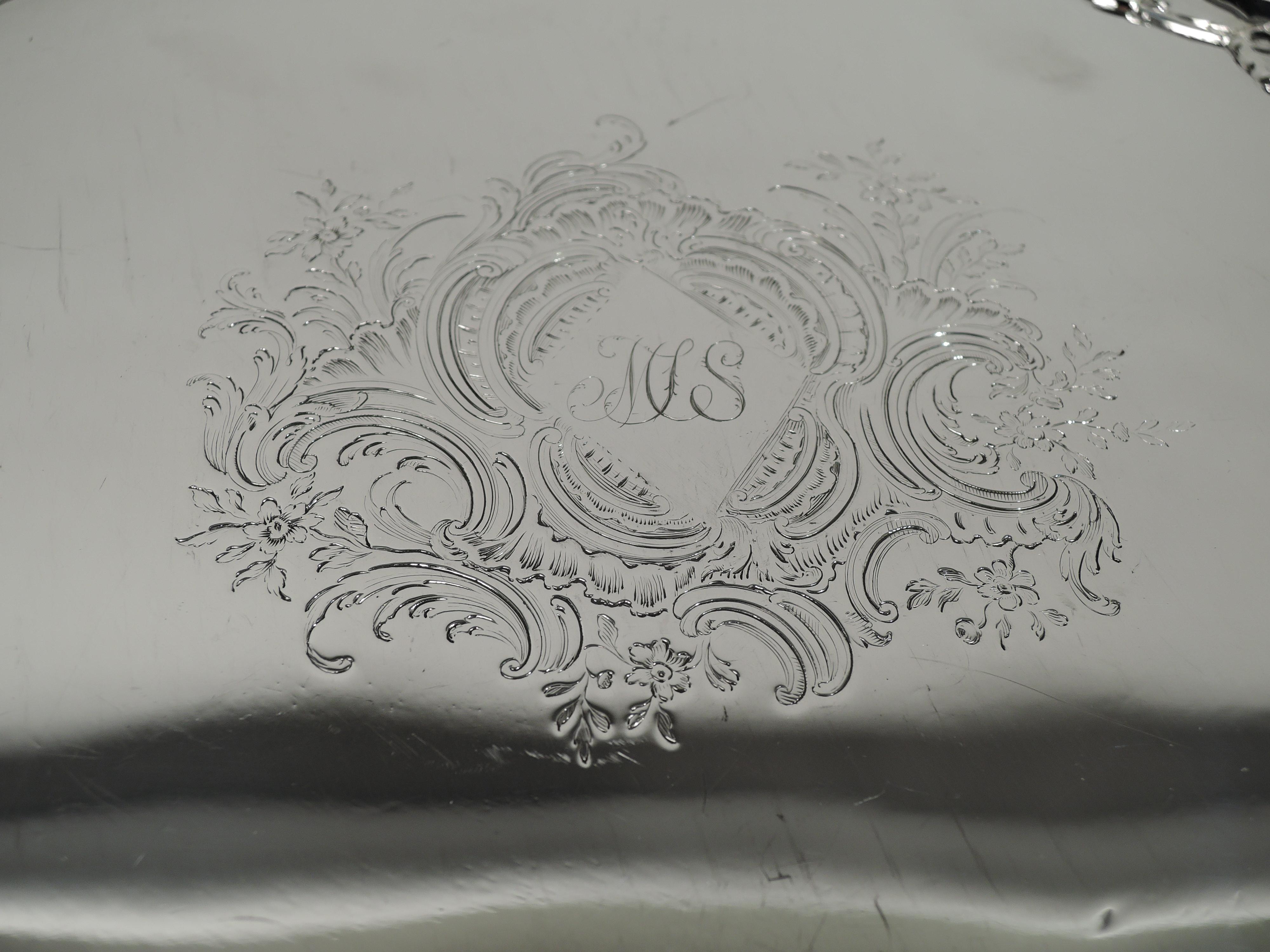 George II sterling silver salver. Made by Richard Rugg in London in 1755. Round with cast serpentine shell-and-leaf rim and 3 leaf-capped volute scroll supports. Well center has lozenge with engraved interlaced script monogram in leafing and