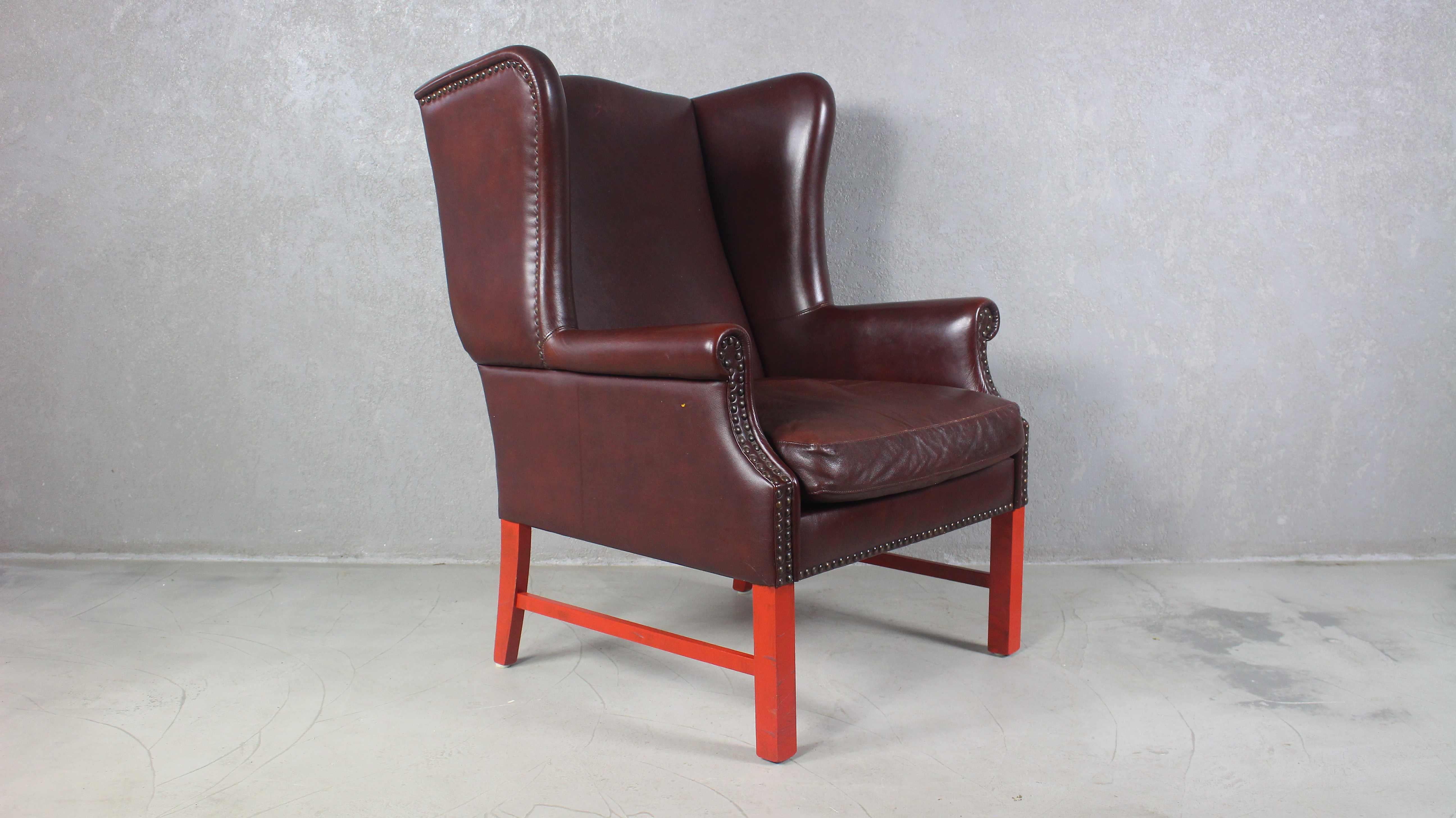 English George III style wingback armchair finished in brown leather. 
The wing chair features fully developed wings and is accented by brass tack nail heads on the borders.