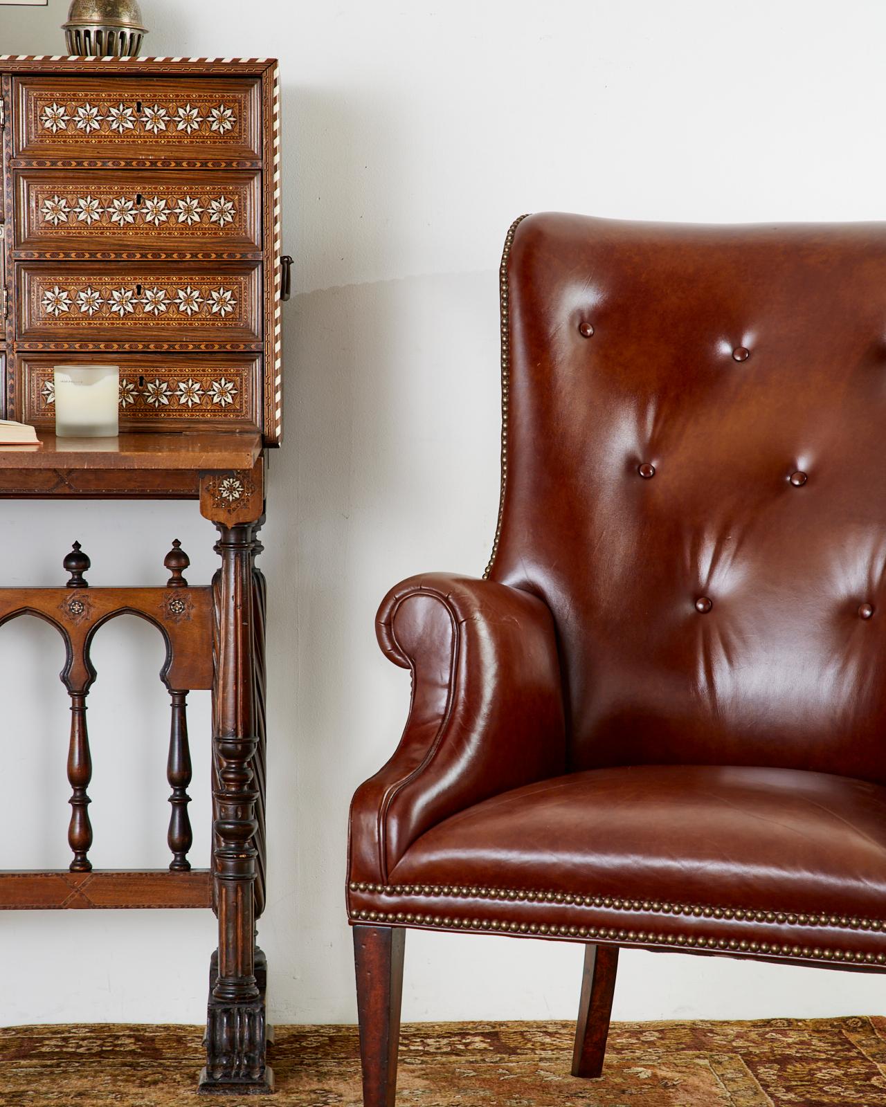 Stylish leather library chair or wingback chair made in the English Georgian taste. Features a supple cognac leather with a tufted back. The chair has Classic rolled arms and is accented by brass tack nailheads on the borders. The hardwood frame is