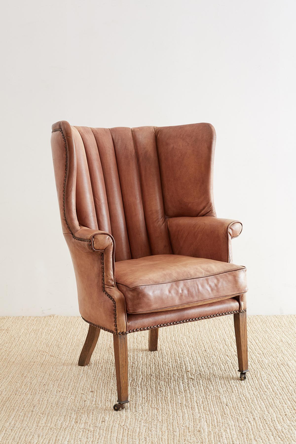 Distinctive leather wing chair or porter's chair made in the English Georgian taste. Features a barrel back design with a channelled back support. The leather frame is bordered by brass nailhead trim and fitted with a loose cushion. The thick