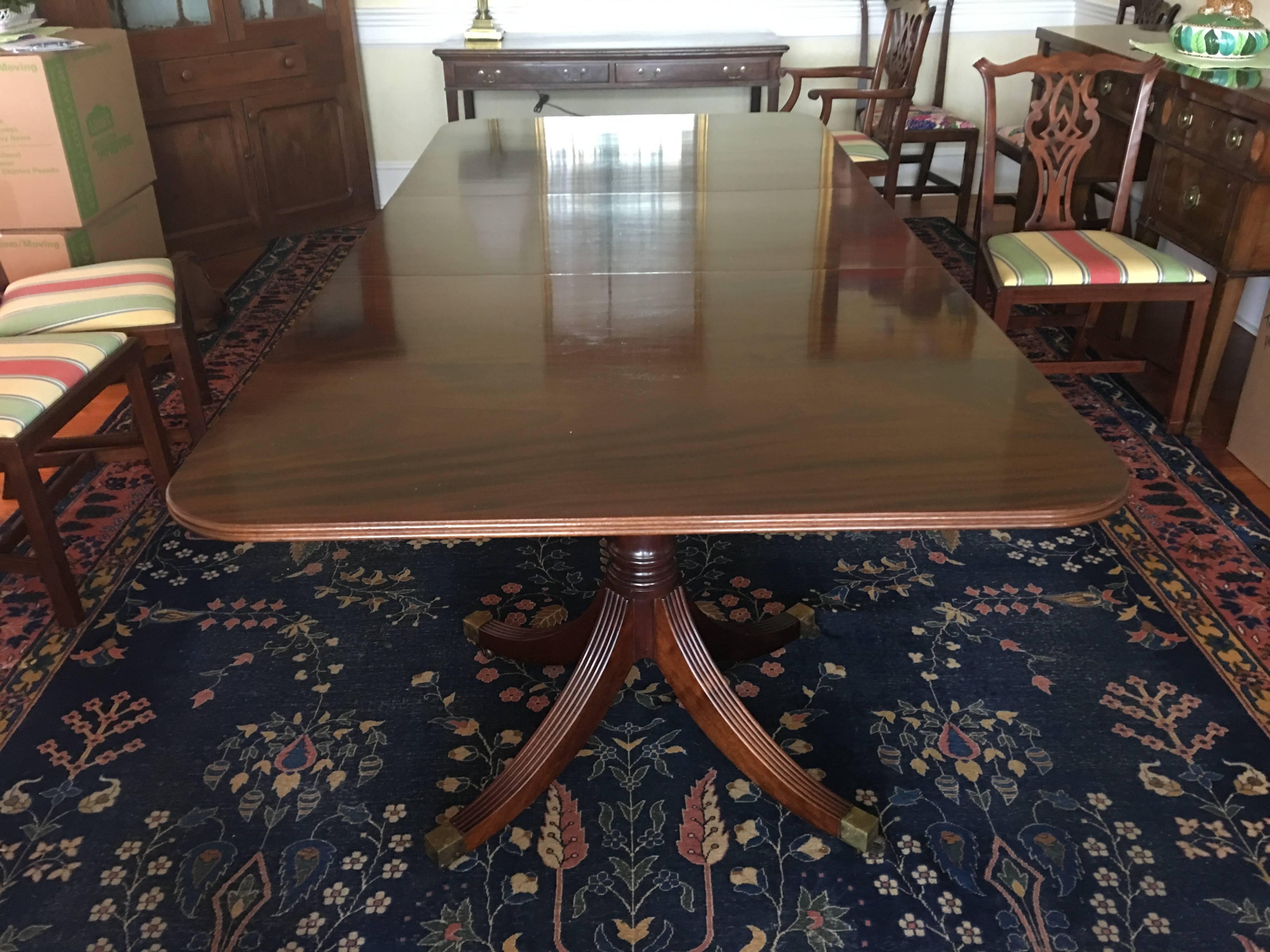 English Georgian style mahogany banquet or dining table with two leaves, early 20th century. It features a molded rounded rectangular top, surmounting a pair of twin pedestals with baluster-turned columns riding upon four out swept reeded legs,