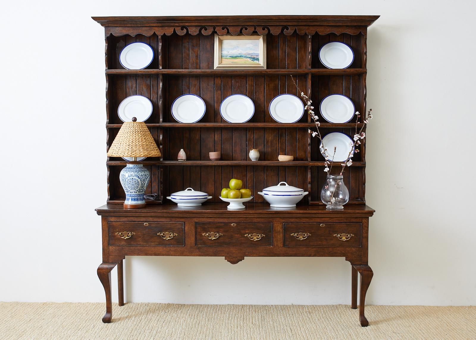 Handsome English oak welsh cupboard with dresser crafted in the Georgian taste. Finely made two-part cabinet having a corniced top and a shaped frieze. Three large shelves for plate storage on top supported by a three-drawer dresser. Each drawer