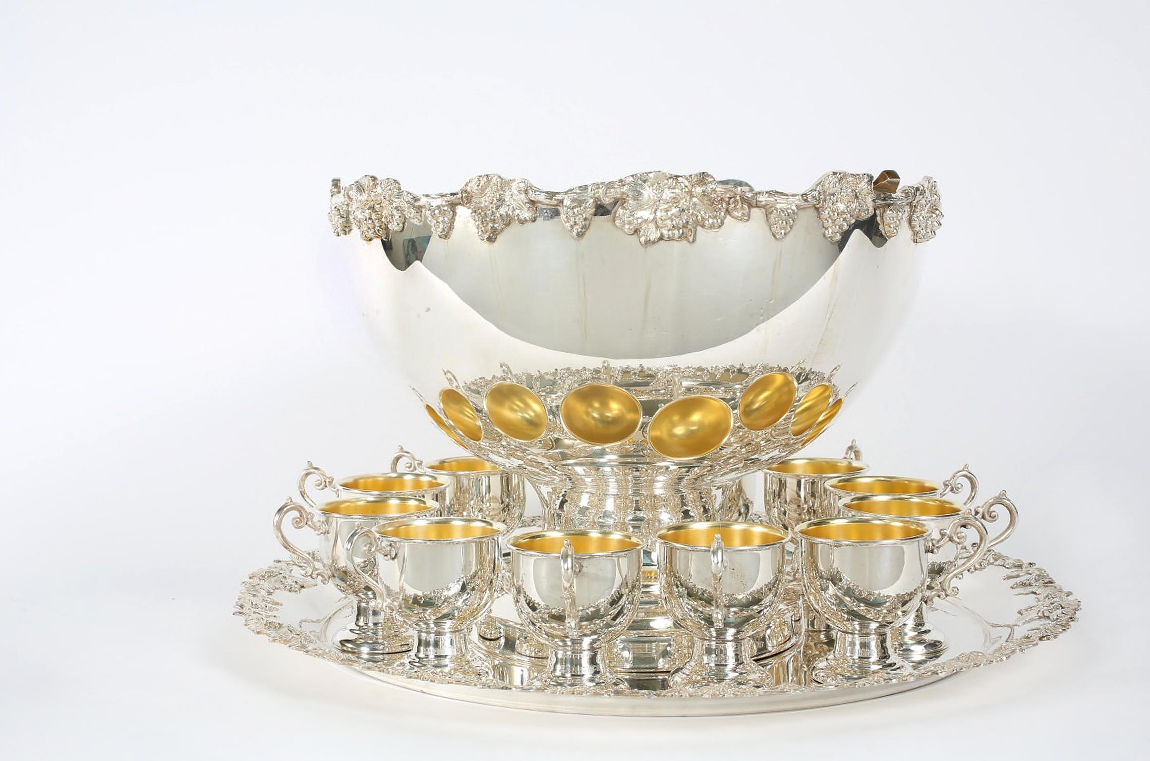 English Georgian style silver plated or copper fifteen piece punch bowl service, complete with twelve decorative cups with gold wash interior and sterling ladle. The bowl with round holding serving tray are highly decorated with incorporating