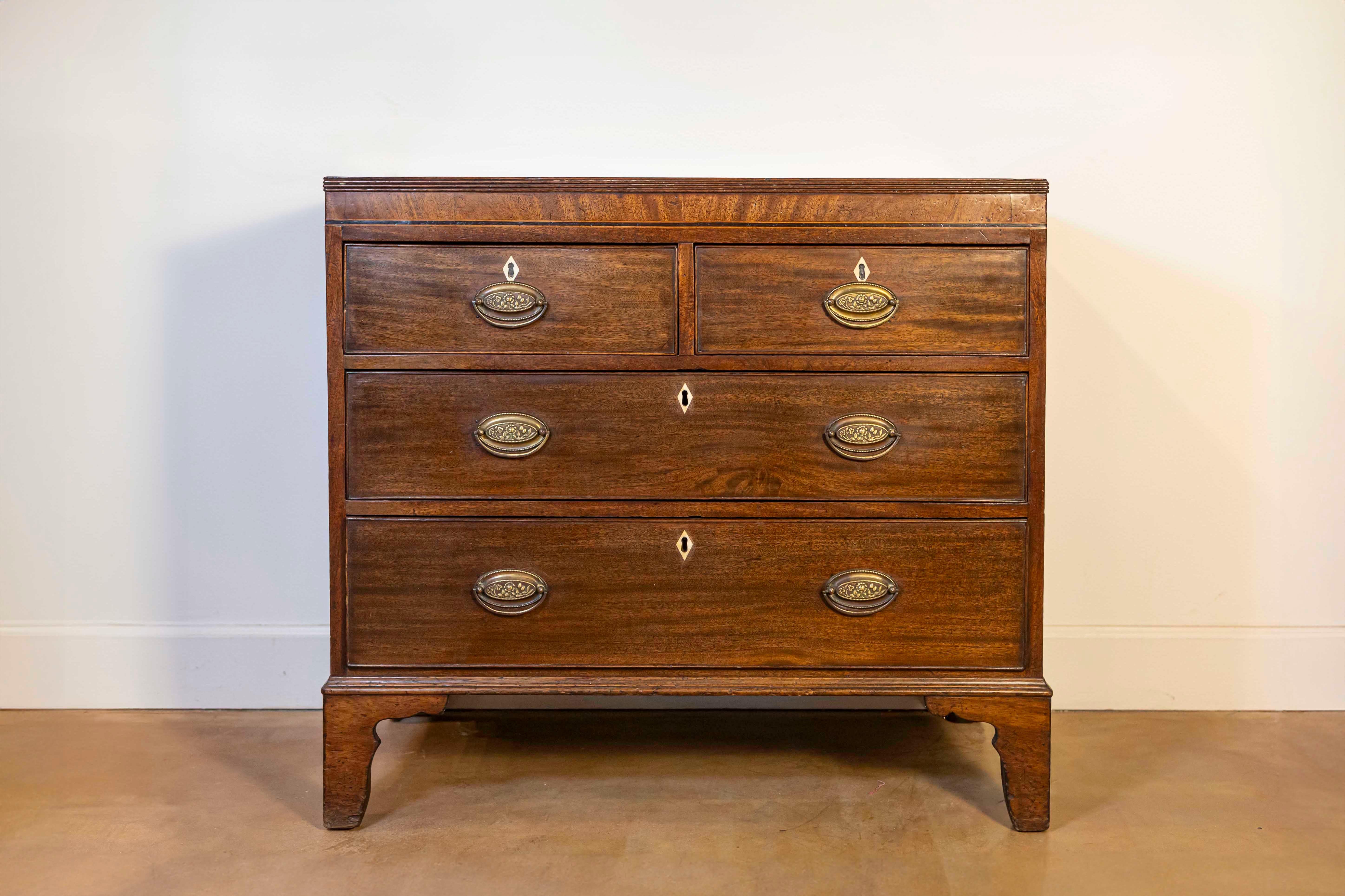 An English Georgian style walnut four-drawer chest from the 20th century with carved legs. This exquisite English Georgian style walnut four-drawer chest, dating back to the 20th century, exudes elegance and fine craftsmanship. Originating from a