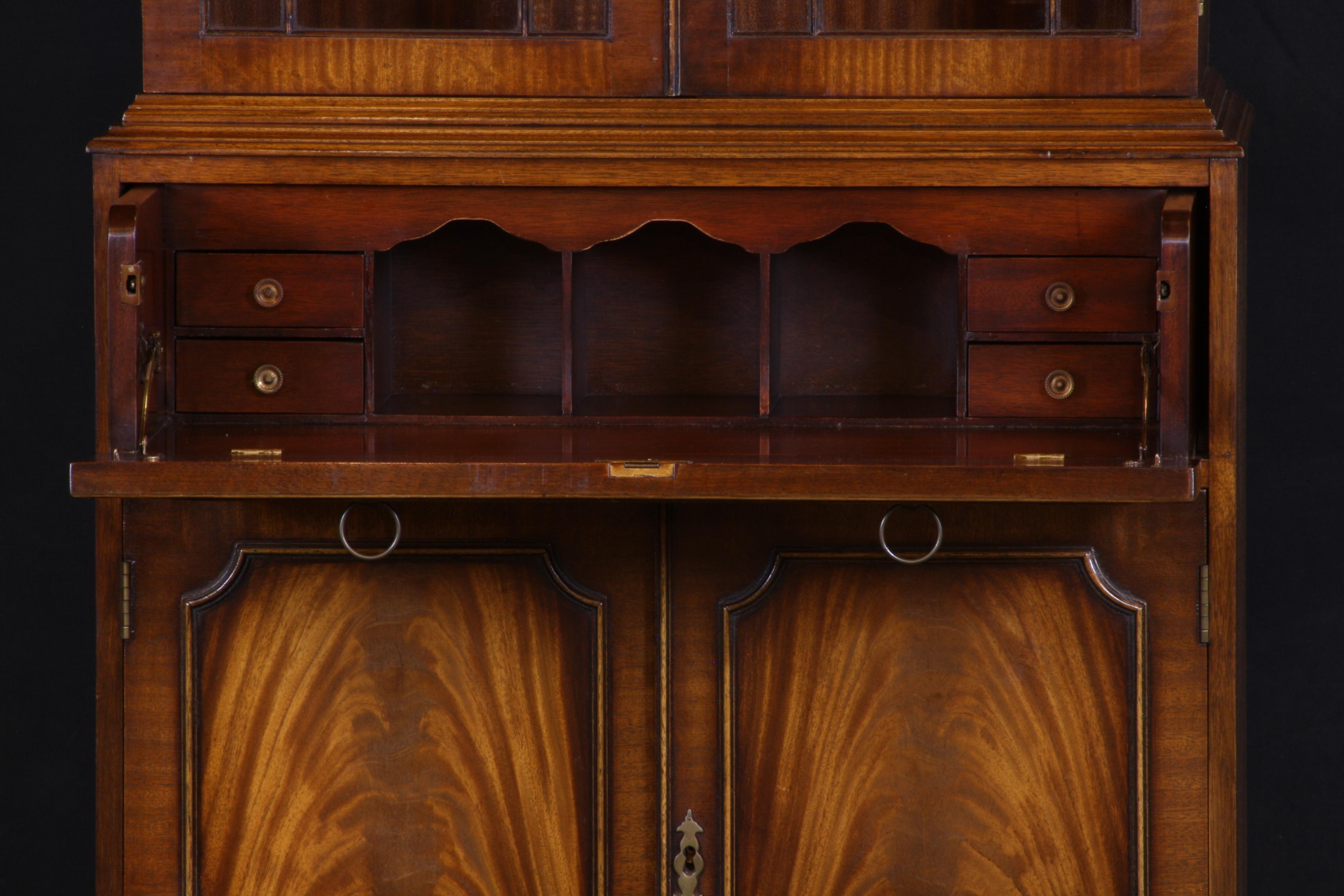 English bookcase with secretary desk in mahogany, Georgian styling, with flamed mahogany and brass fittings. The glass doors are hand glazed with individual panes of glass. A drop front drawer reveals a compact desk compartment for the organized
