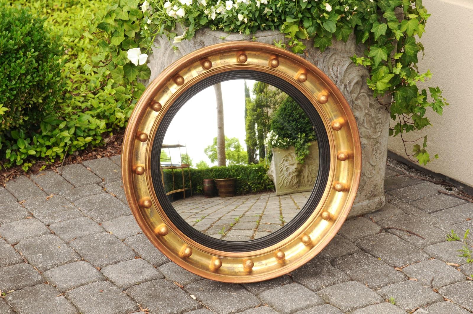An English giltwood bullseye convex girandole mirror from the late 19th century with ebonized reeded accents. Born in England during the third quarter of the 19th century, this stylish circular mirror features a convex mirror plate, surrounded by a