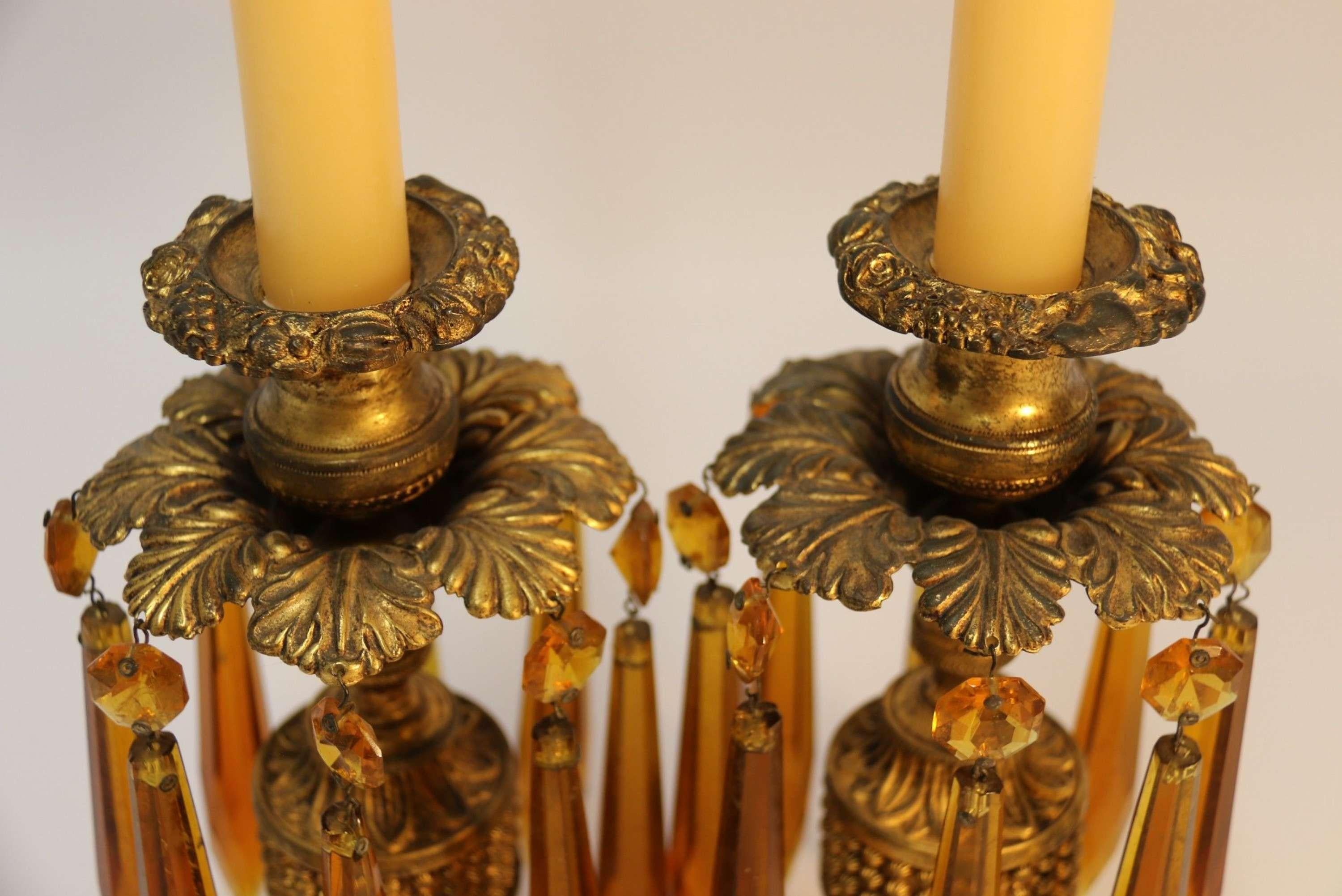 A fine pair of Regency Luster Candlesticks

A rare pair of English late Regency period weighted gilt brass and embossed candlesticks with the most unusual amber cut glass hanging lusters. They are in good original condition with original gilt