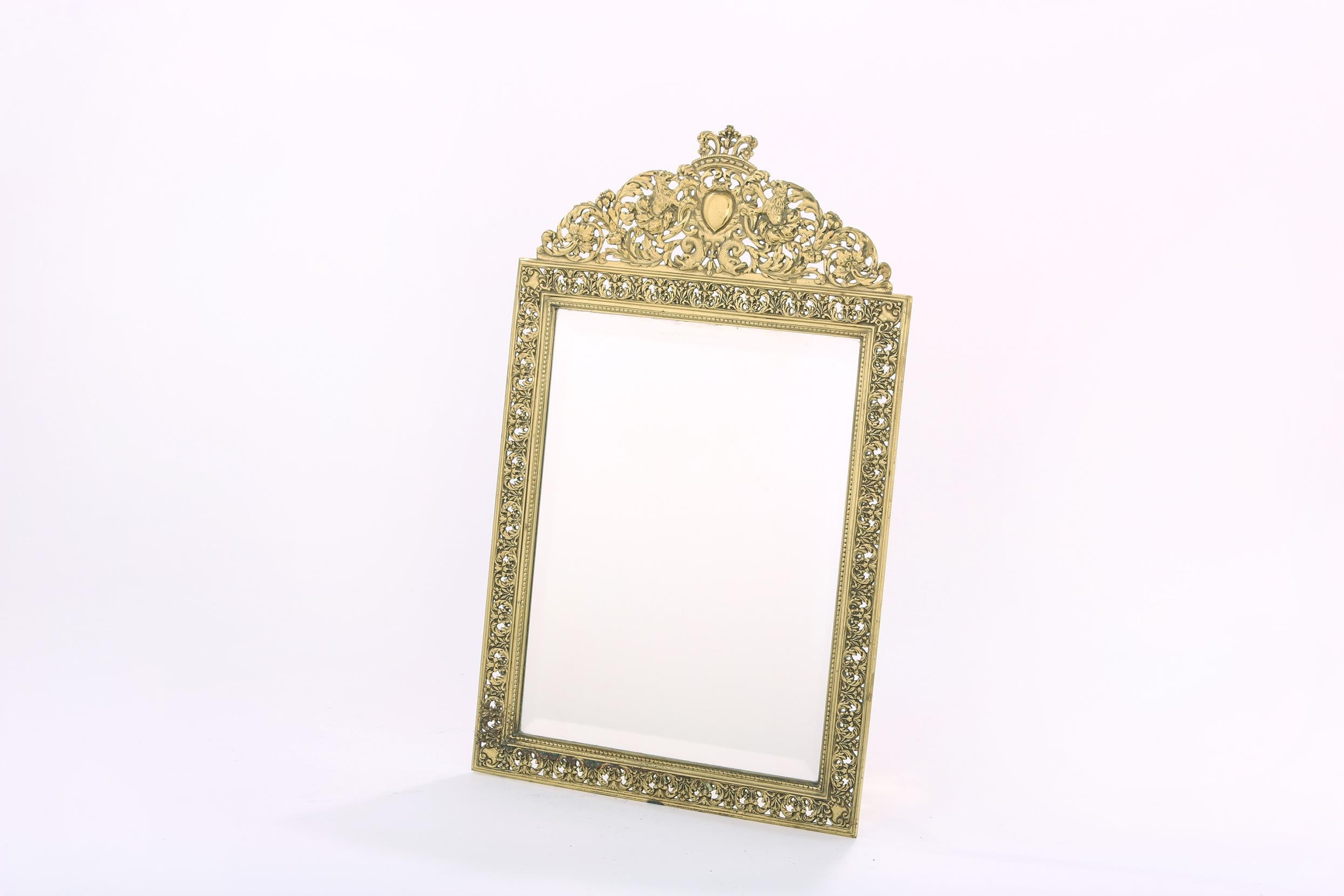 English gilt brass framed beveled vanity mirror with exterior design details. The mirror is in good condition. Minor wear appropriate with age / use. Maker's mark undersigned. The vanity mirror stand about 20.5 inches tall X 12.5 inches wide. The