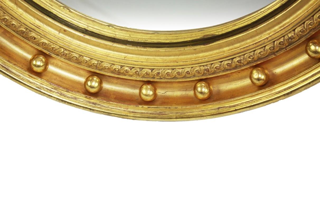 English gilt convex mirror with stepped and rounded outer rim surrounding a deep corvetto filled with ball decoration. Inner edge has woven band finished with a concave slip holding the convex plate.
  