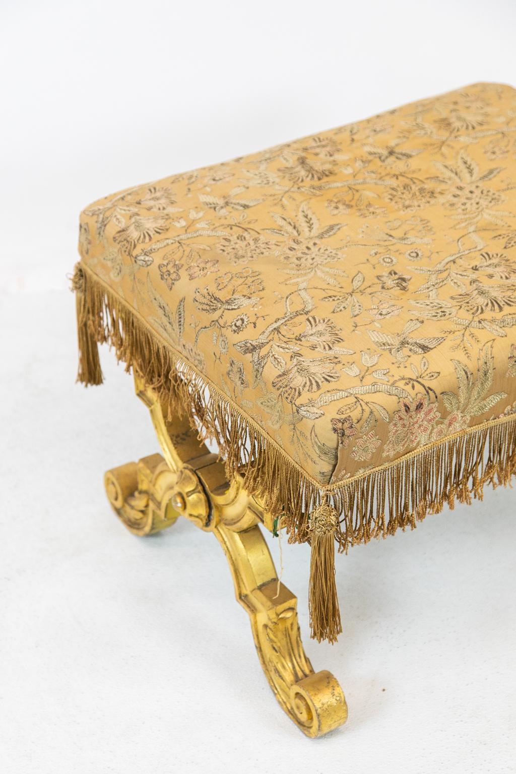 English gilt stretcher stool has a turned spiral support stretcher. The upholstery is original and has wear and light stains.
 