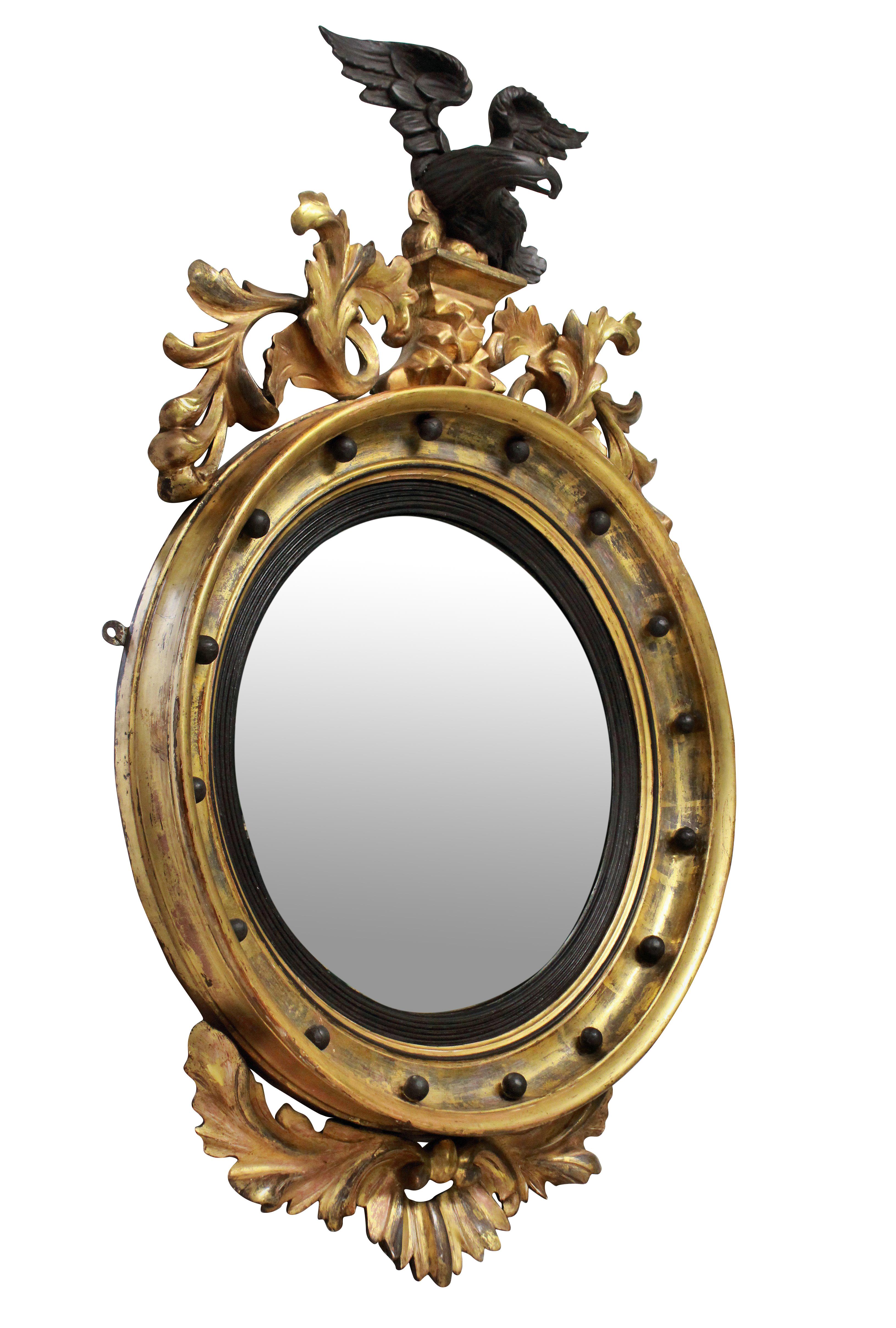 A lovely 19th century circular gilded convex mirror with ebonized slip, surmounted with an ebonized cresting carved eagle with a carved foliate apron.
 