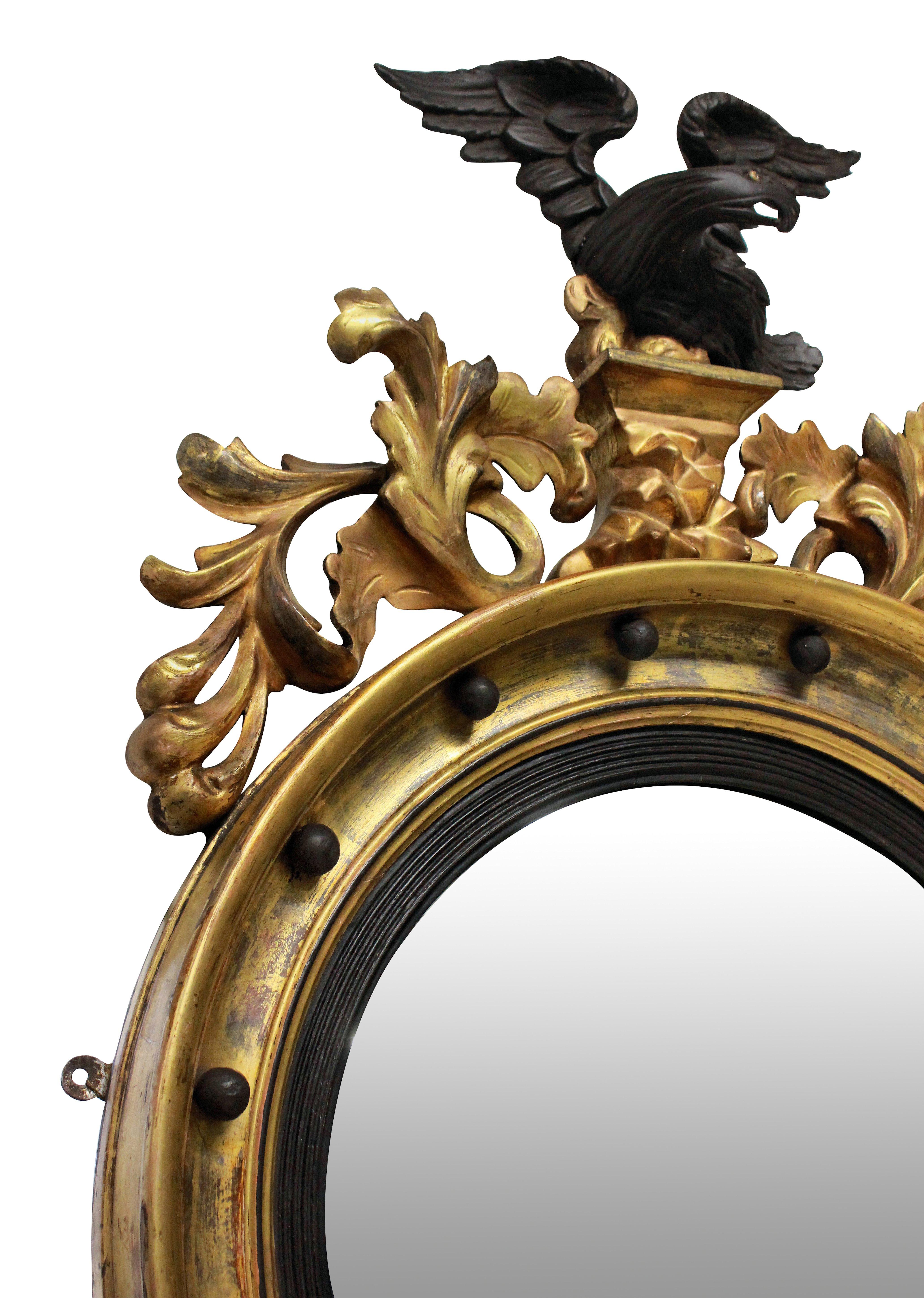A lovely 19th century circular gilded convex mirror with ebonized slip, surmounted with an ebonized cresting carved eagle with a carved foliate apron.
 