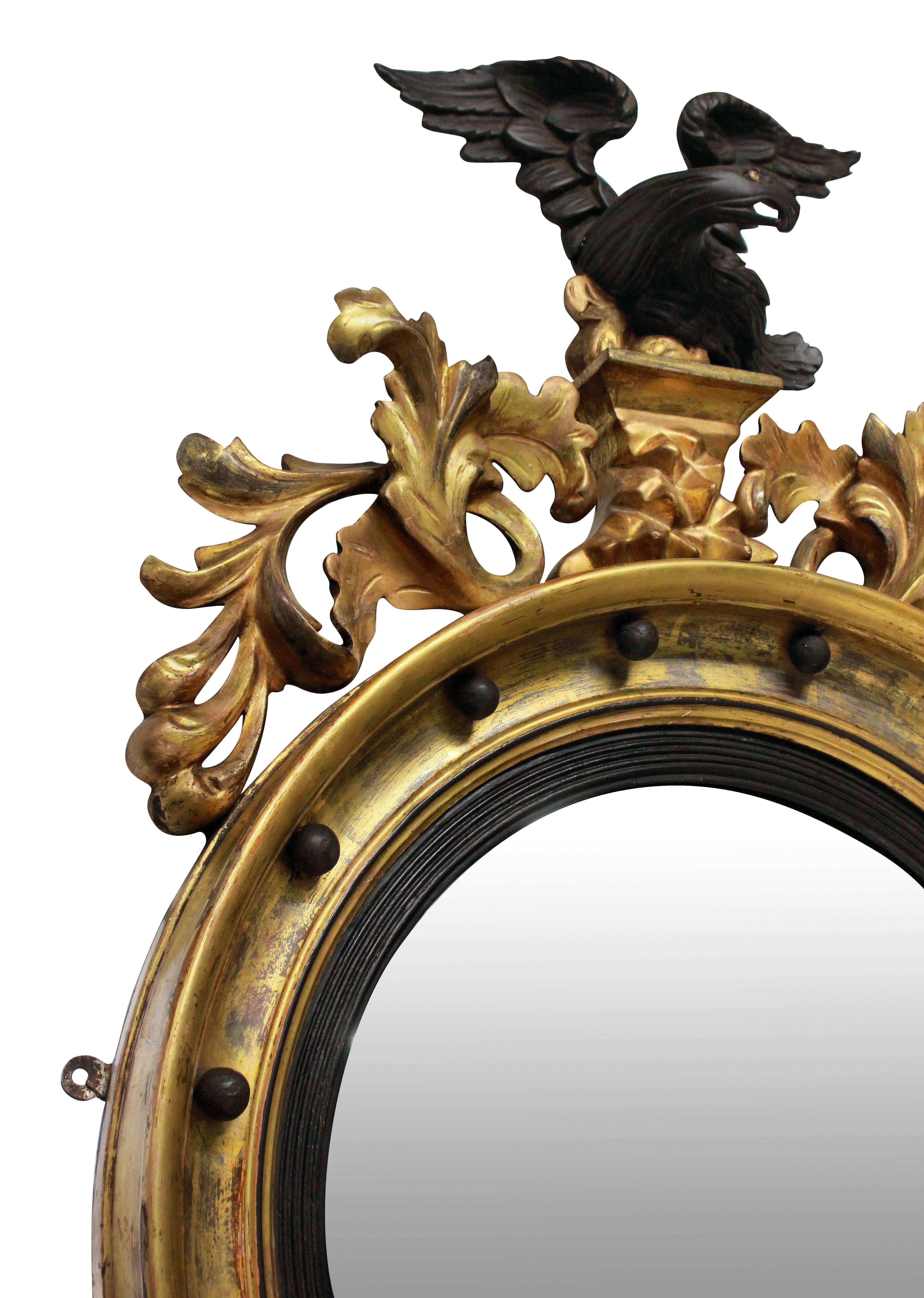 A lovely 19th century circular gilded convex mirror with ebonized slip, surmounted with an ebonized cresting carved eagle with a carved foliate apron.
  