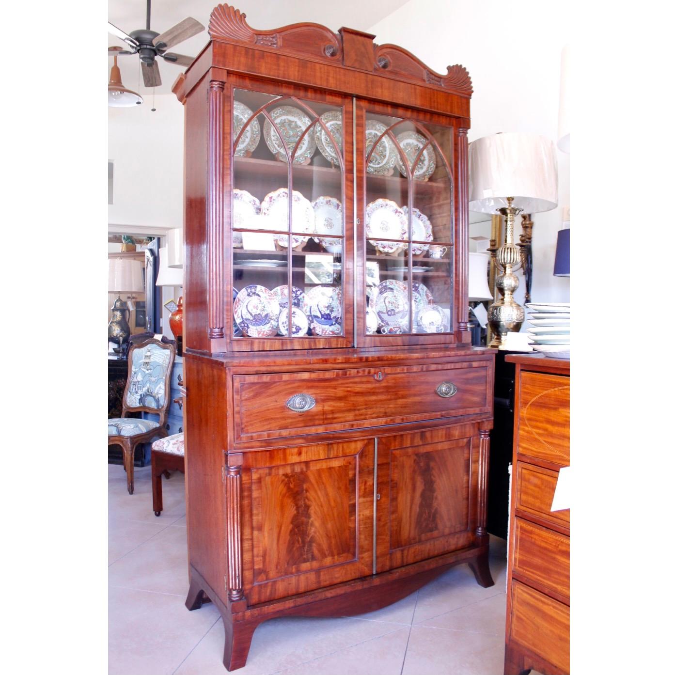 A stylish English mahogany William IV period piece, (ca. 1830), with a strikingly arched cornice terminating in half palmettes. Arched tracery distinguishes the glass doors of the top display cabinet, and the interior of the cabinet below is fitted