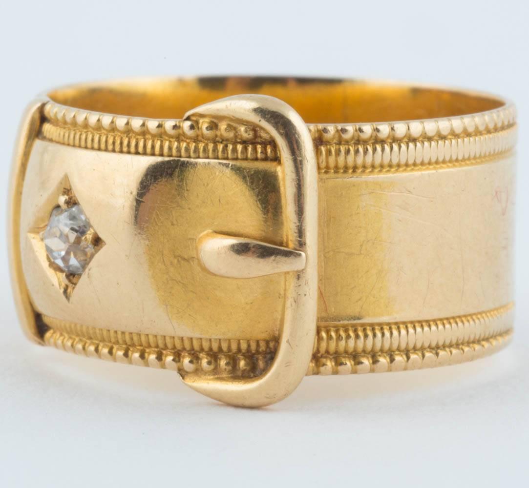 And elegant wide band of polished 18k yellow gold within textured borders, the top designed as a belt buckle set with an antique-cut diamond.  

With London hallmarks and maker’s mark JG.  

Size 8 1/2.  Width of band: 3/8 in (1 cm).


