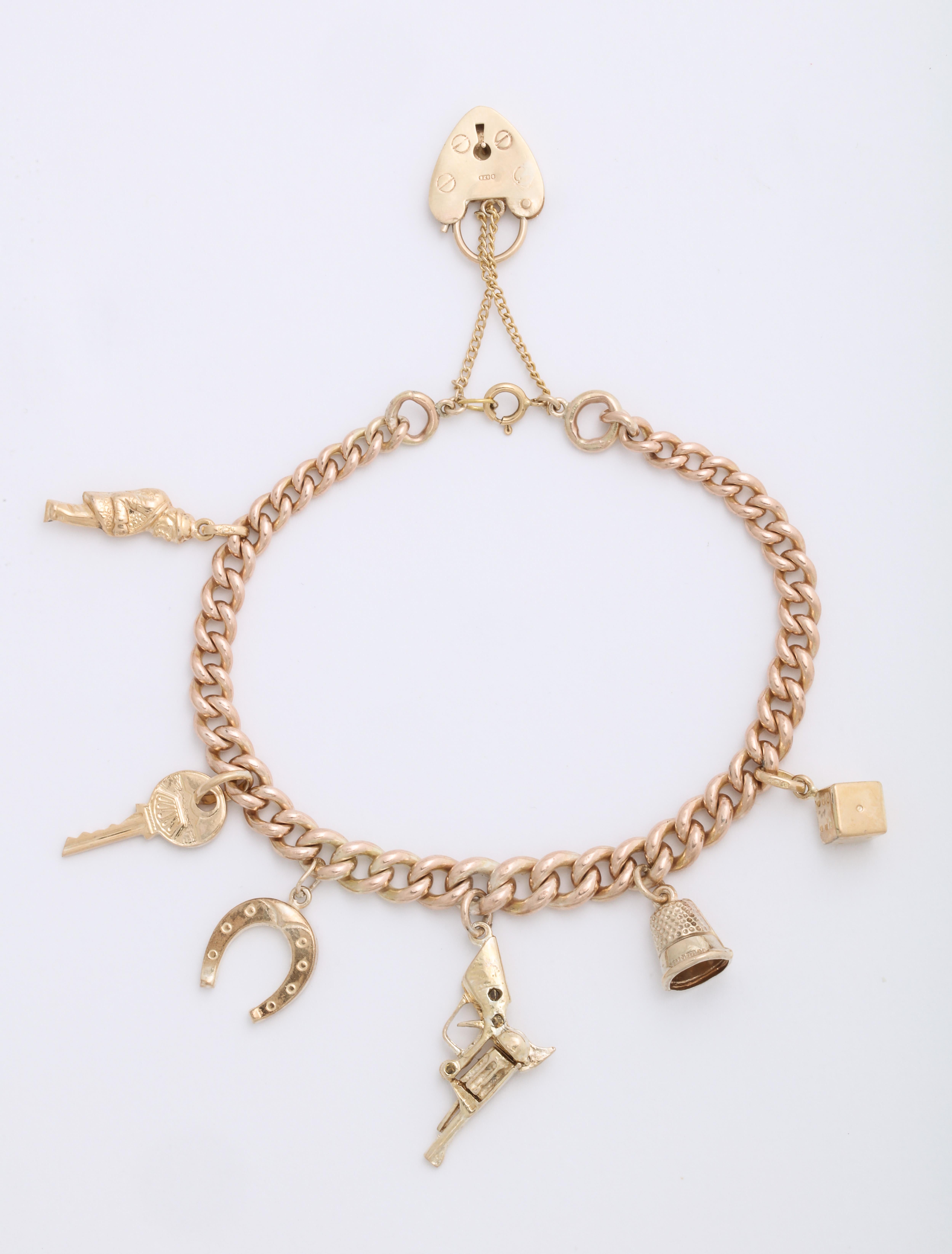 An English vintage gold charm bracelet, of 9k rose gold swedge links terminating in a 9k rose gold heart-shaped  clasp, suspending yellow gold charms in 18k and 9k gold: a single die, thimble, pistol, horseshoe, key stamped apre il tuo cuore (open