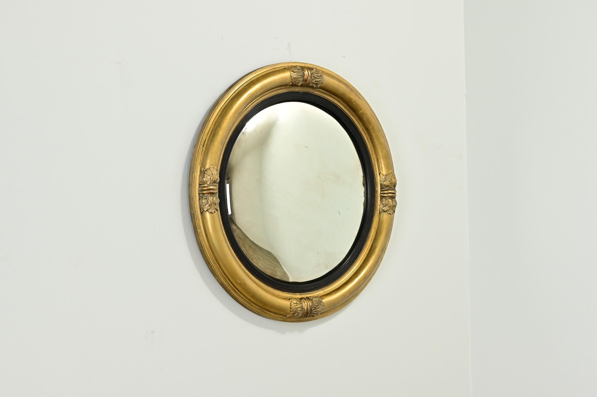 An elegant English gold gilt convex mirror. The antique convex mirror plate is surrounded with an ebonized trim and a gold gilt frame with four carved designs. Fixed with a circular bracket and ready to be hung in your interior. Make sure to view