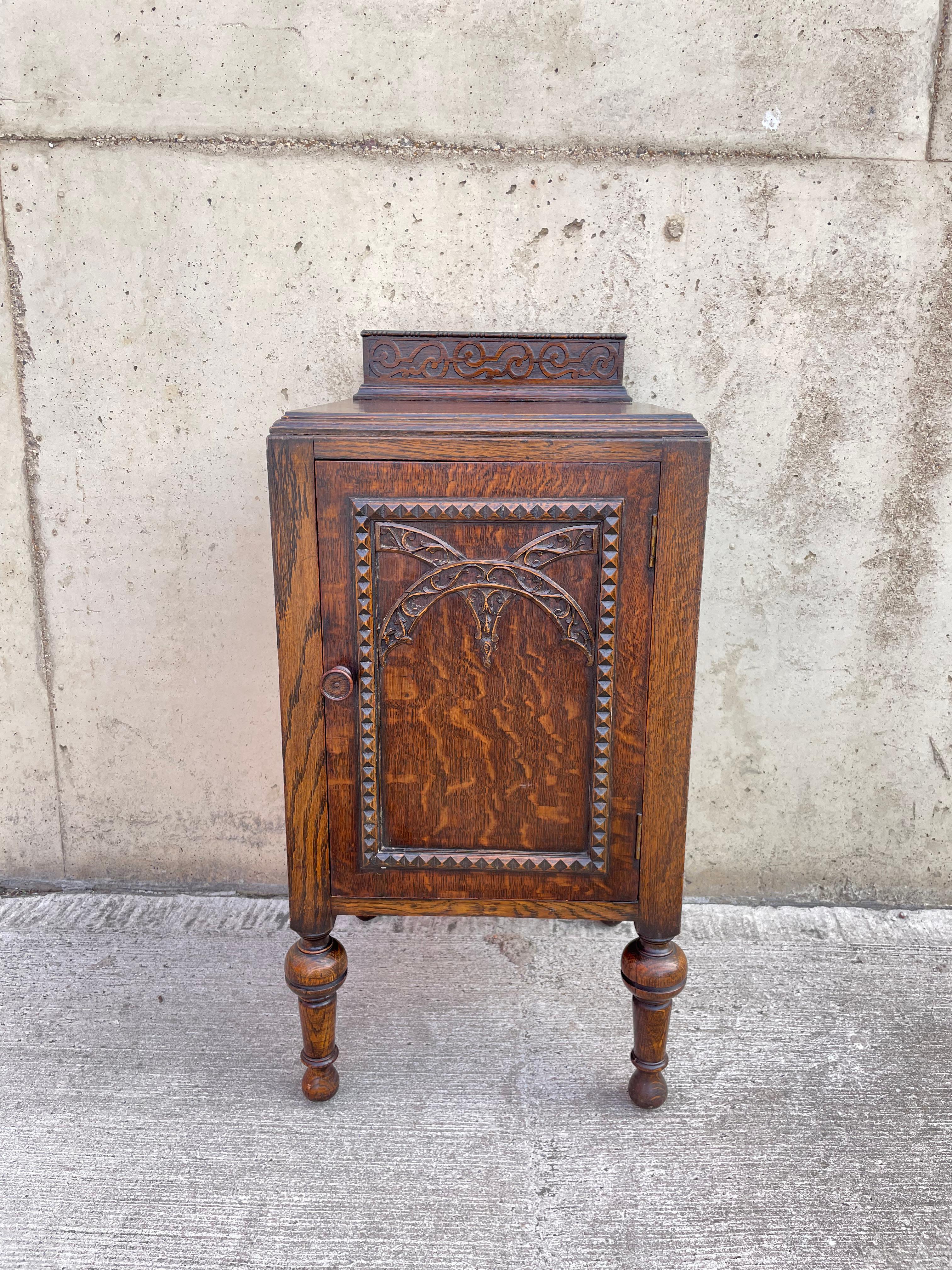 Mobile inglese in rovere tigrato con splendidi dettagli intagliati a mano e alte gambe tornite. Il mobile presenta un architrave intagliato nella parte superiore e un'anta intagliata a mano con un design brutalista. All'interno del mobile c'è un