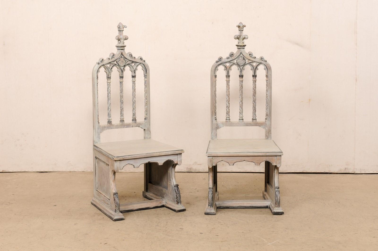 An English pair of Gothic Revival style carved and painted wood chairs, circa 1920's. This antique pair of chairs from England have been intricately carved in Gothic Revival style with classic arched back adorn with tall spire finials, and