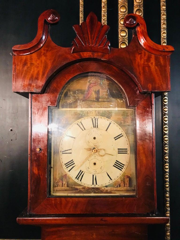 English floor clock from the 19th century, mahogany with defects, hand painted dial with Roman numerals and polychrome painting with vedute painting. The movement may not work; it may have to be taken to a watchmaker.