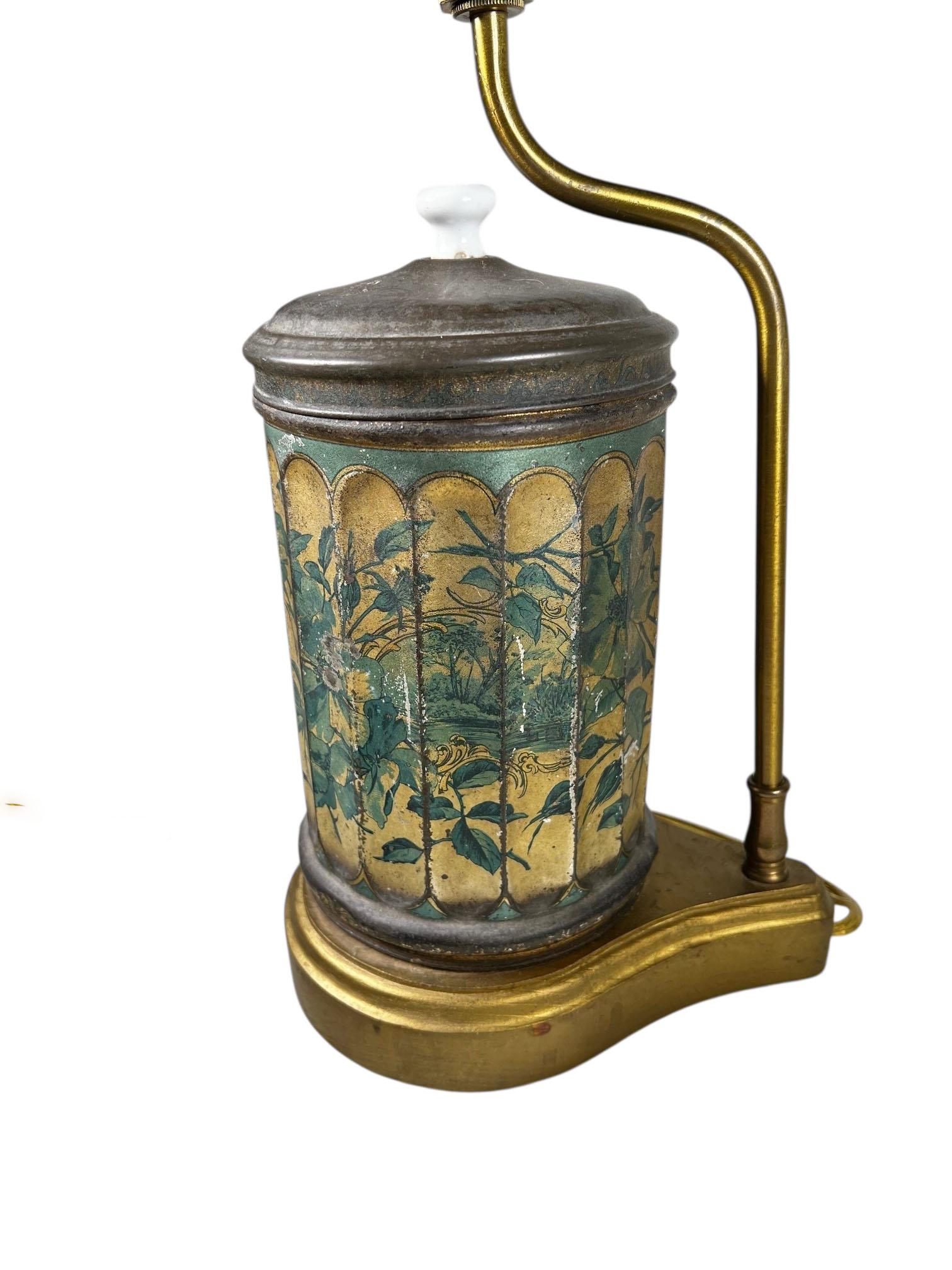 A striking green tole tea canister lamp from England, transformed into a one of a kind lighting piece. The canister features classic beveled sides and rests on a custom stand, with a coordinating shade trimmed in a complementary custom border for a