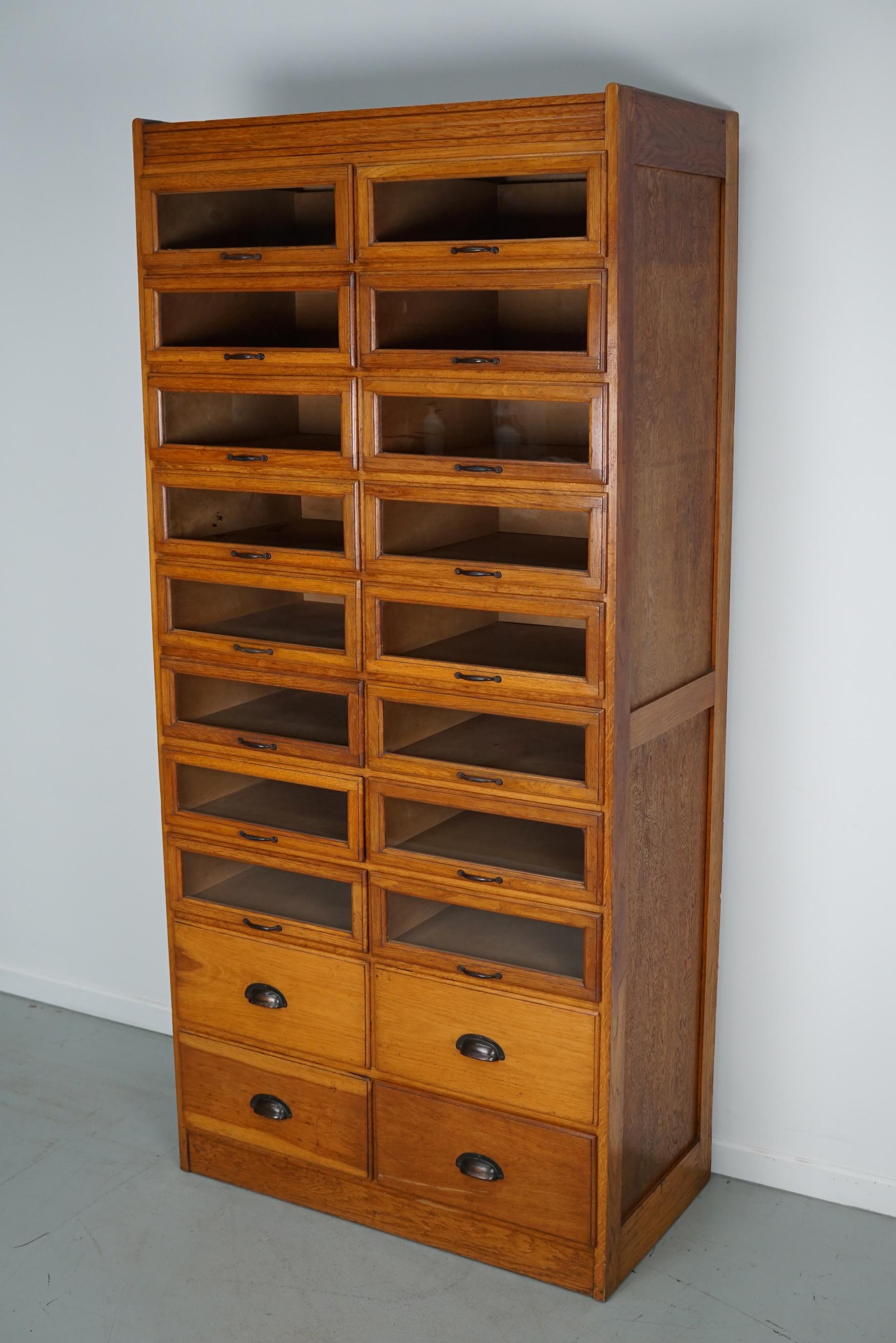 This vintage oak haberdashery cabinet dates from the 1930s and was made in England. It features a solid wooden frame with glass fronted drawers and four large closed drawers at the bottom. The interior dimensions of the drawers are: DWH 41 x 40 x 13