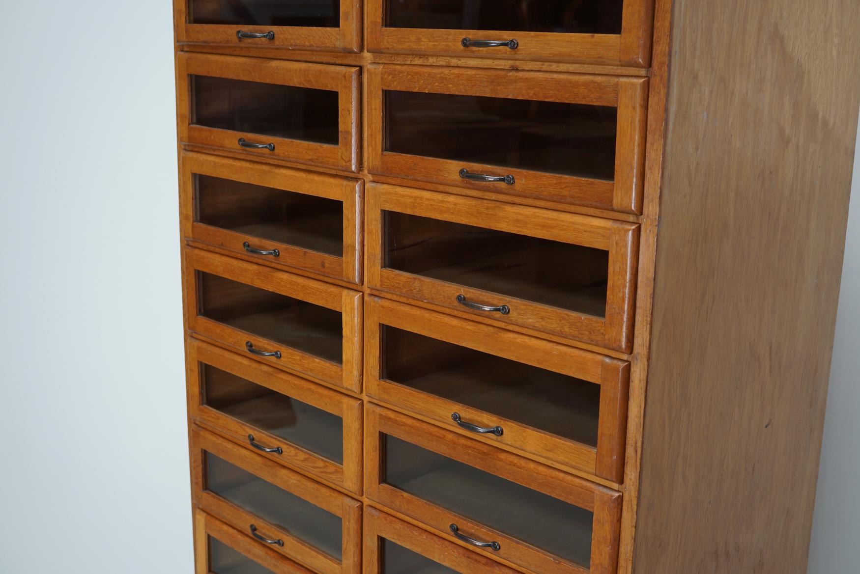 This vintage oak haberdashery cabinet dates from the 1930s and was made in England. It features a solid wooden frame with glass fronted drawers and four large closed drawers at the bottom. The interior dimensions of the drawers are: DWH 40 x 40 x