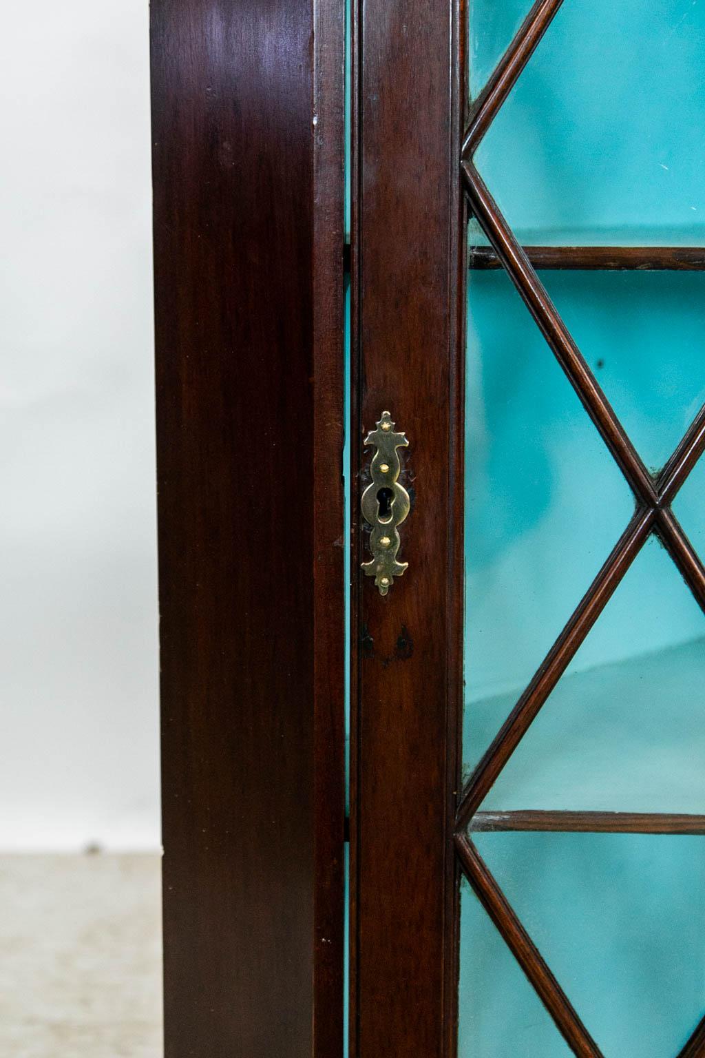 The door of this mahogany corner cupboard has blown wavy glass diamond shaped panes. It has three fixed shelves with a shallow butterfly shape. The interior is painted with a robin's egg blue color except for the front edges of the shelves which