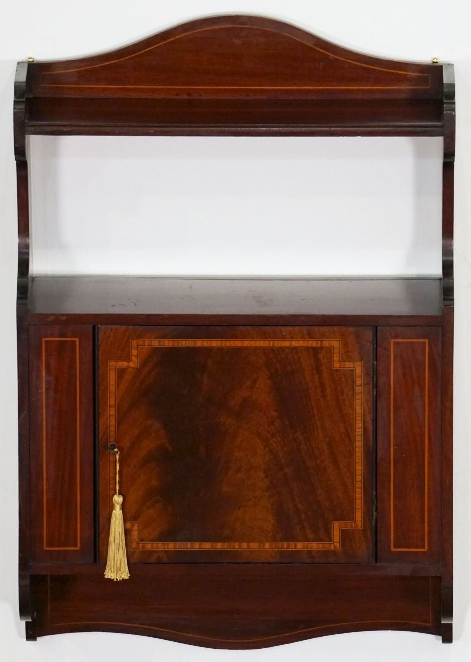 A fine English hanging shelf with or curio cabinet of inlaid mahogany, from the Edwardian period, featuring a decorative serpentine gallery backsplash with inlay above the top shelf, over an inlaid cabinet door that opens to a cupboard for storage,