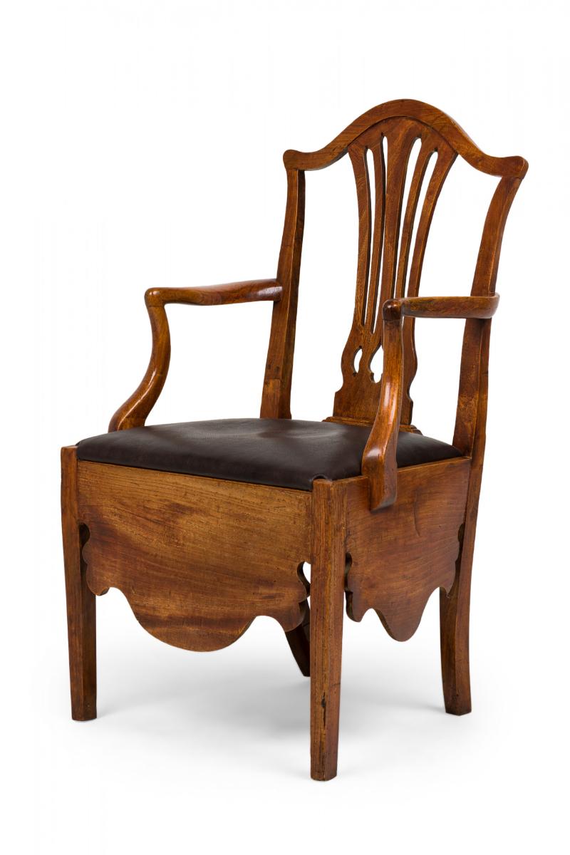 Silla cómoda inglesa Hepplewhite (s. XVIII), de madera de olmo, con respaldo calado en forma de urna ligeramente curvada, brazos perfilados y delantal aplanado que rodea un asiento de cuero negro, ocultando una abertura inferior para un orinal.

El